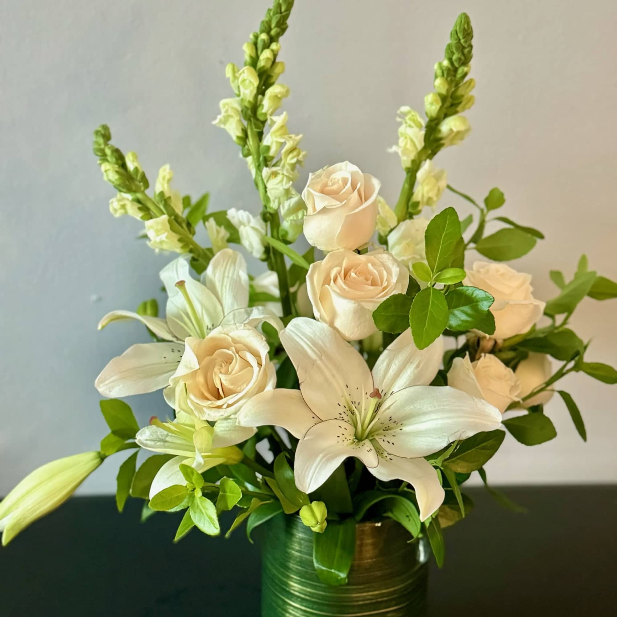 Cream roses and white lilies in a green vase