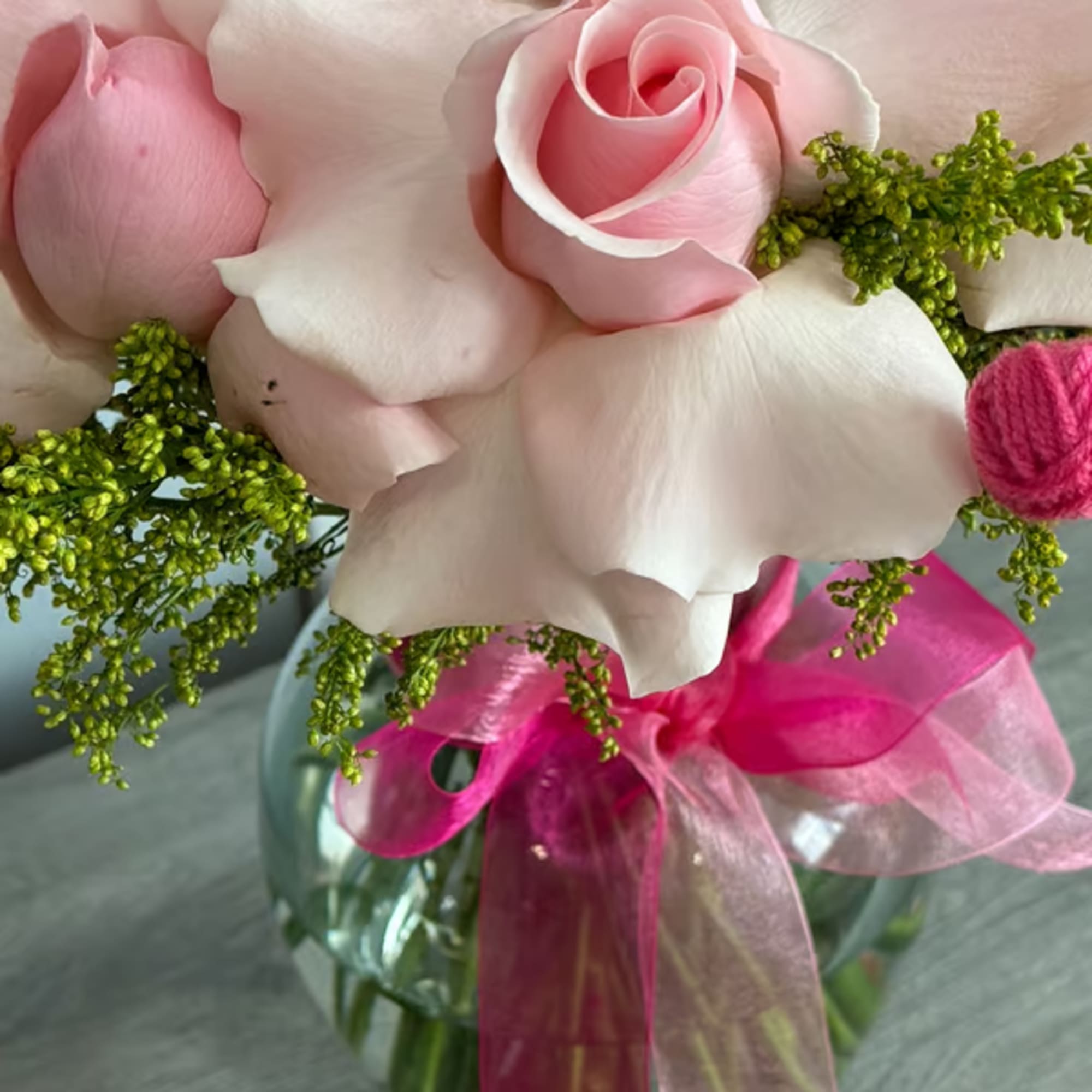 Pink roses arranged in a glass vase with a pink ribbon