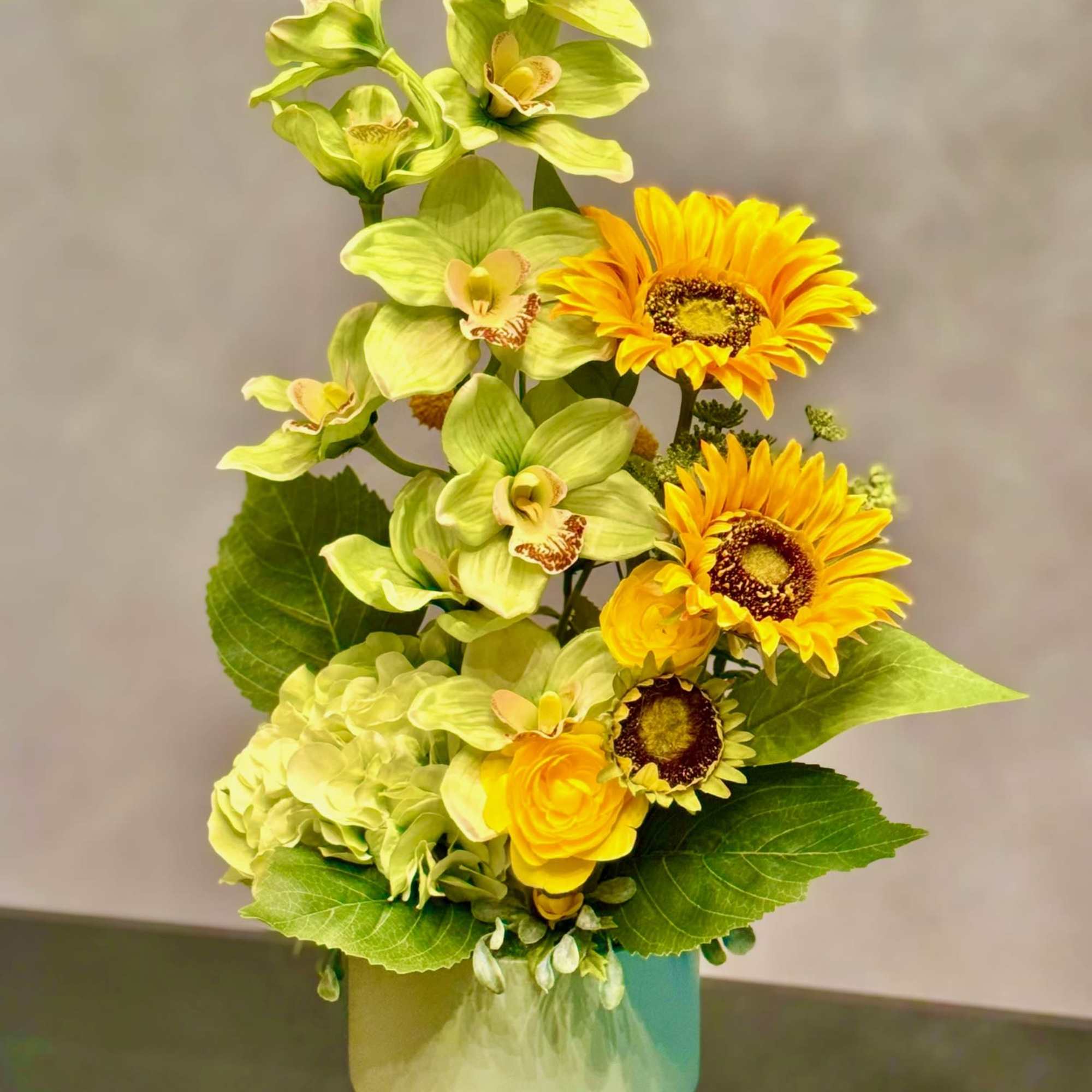 Yellow flowers and green orchids arranged in a pale vase