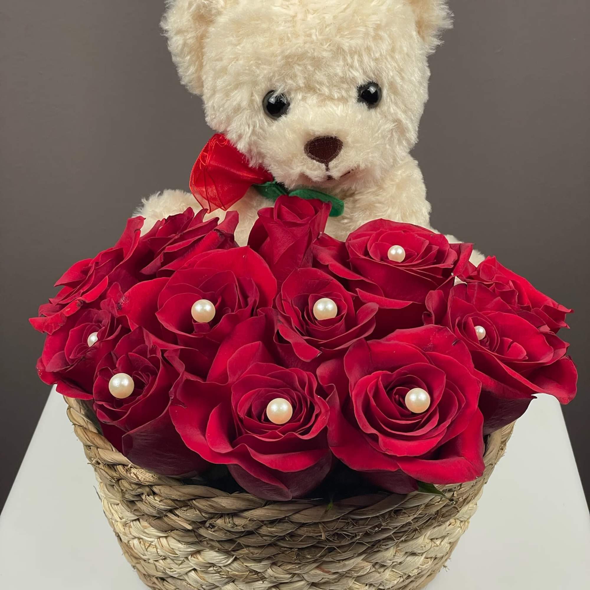 Teddy bear above a basket of red roses with pearl accents