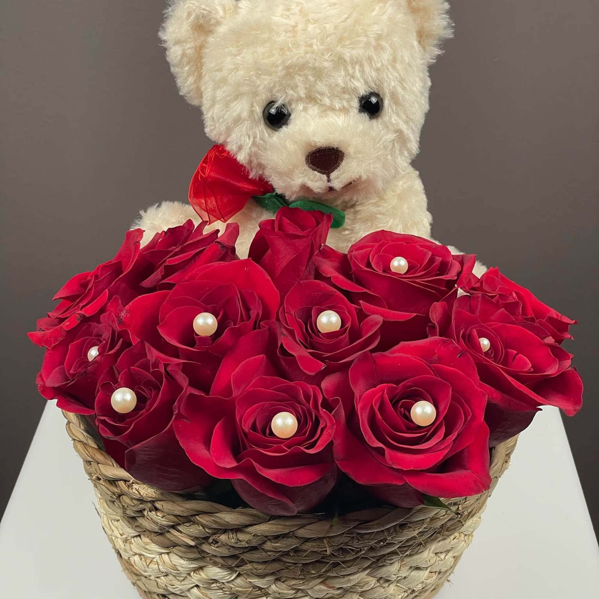Teddy bear above red roses in a woven basket