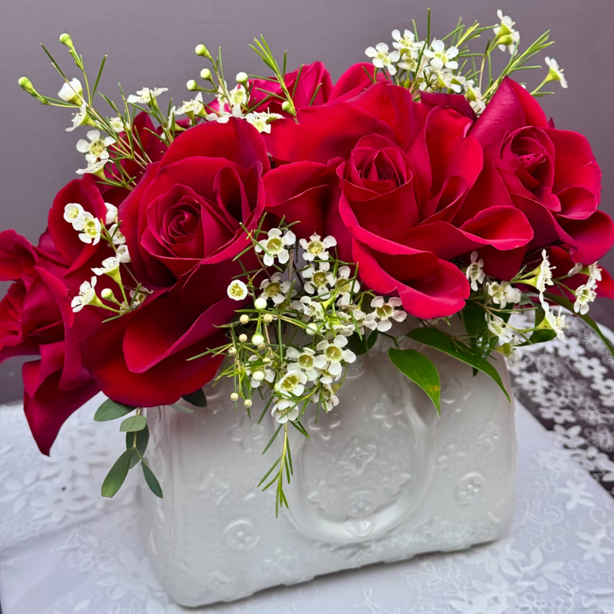 Red rose bouquet with white filler flowers in a white ceramic vase