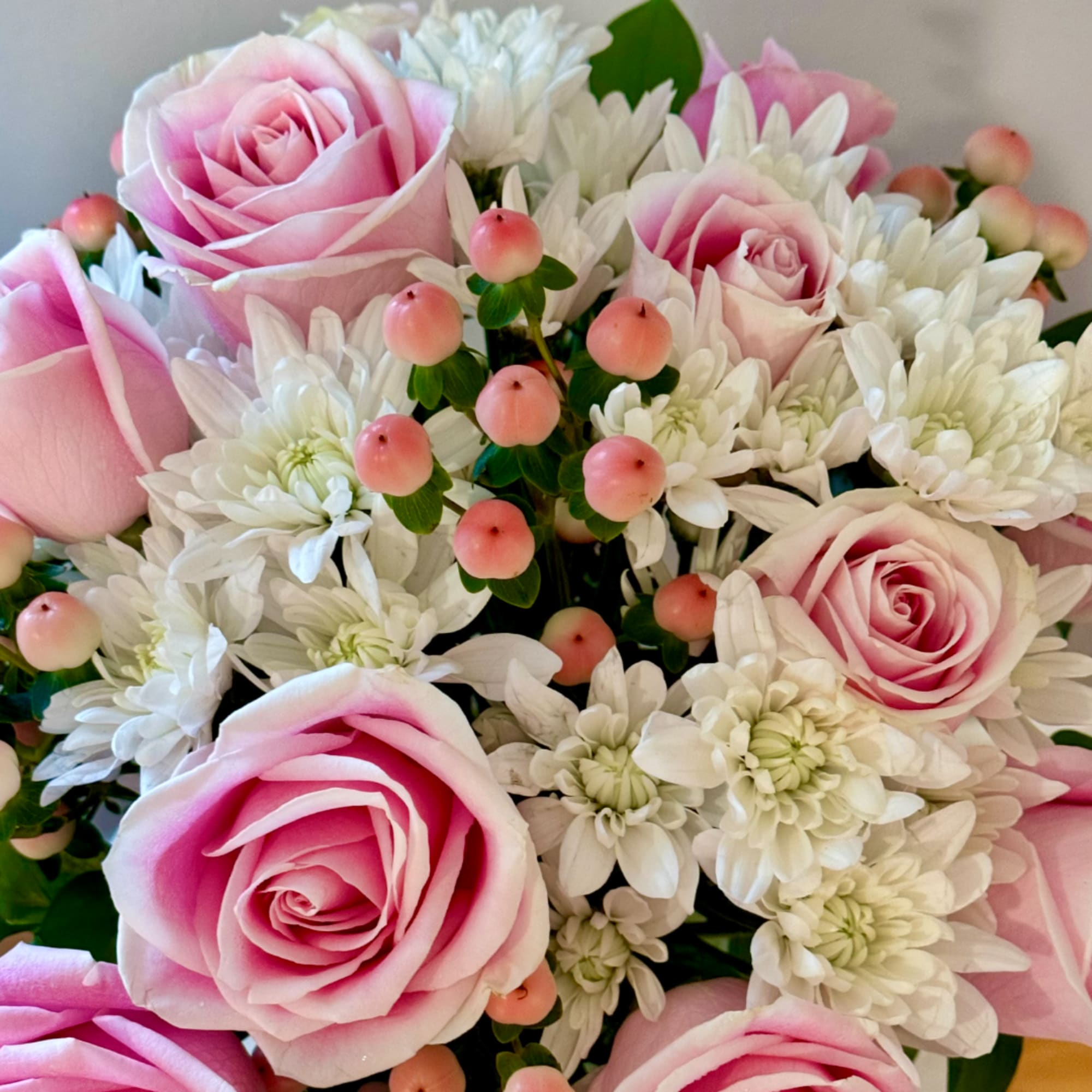 Pink roses with white daisies and small pink berries in a bouquet