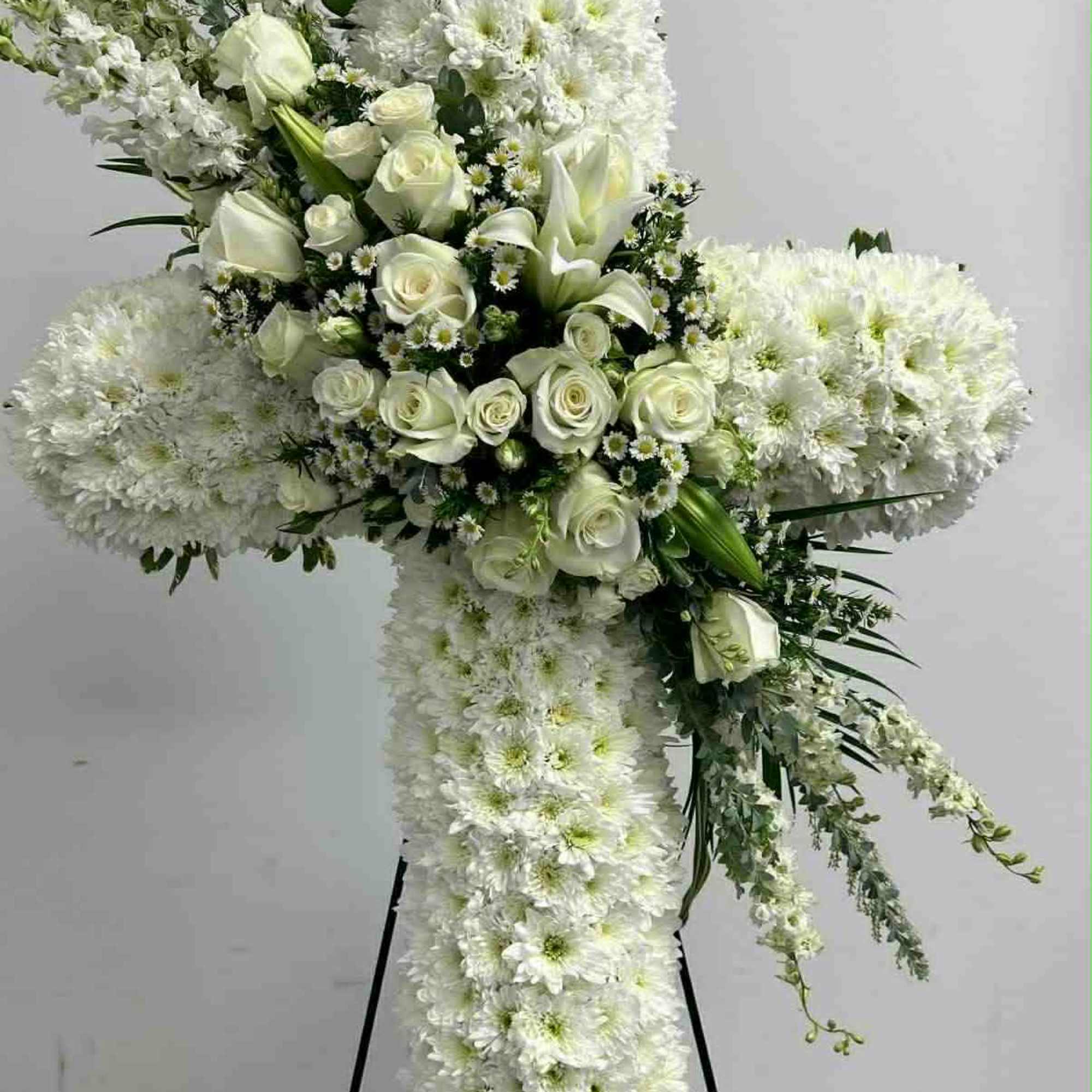 White floral cross on a stand with roses and chrysanthemums
