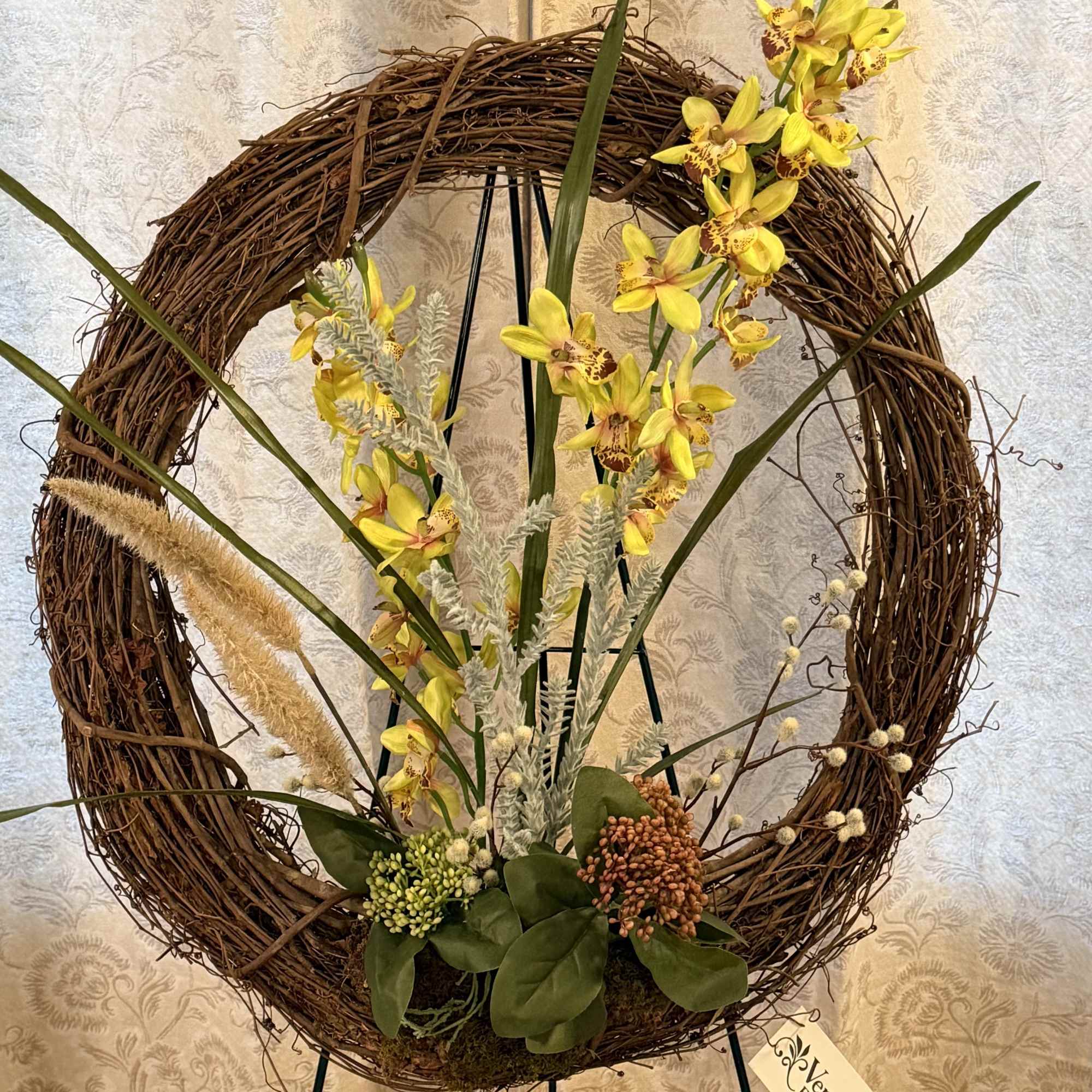 Yellow orchid arrangement in a grapevine wreath on a stand
