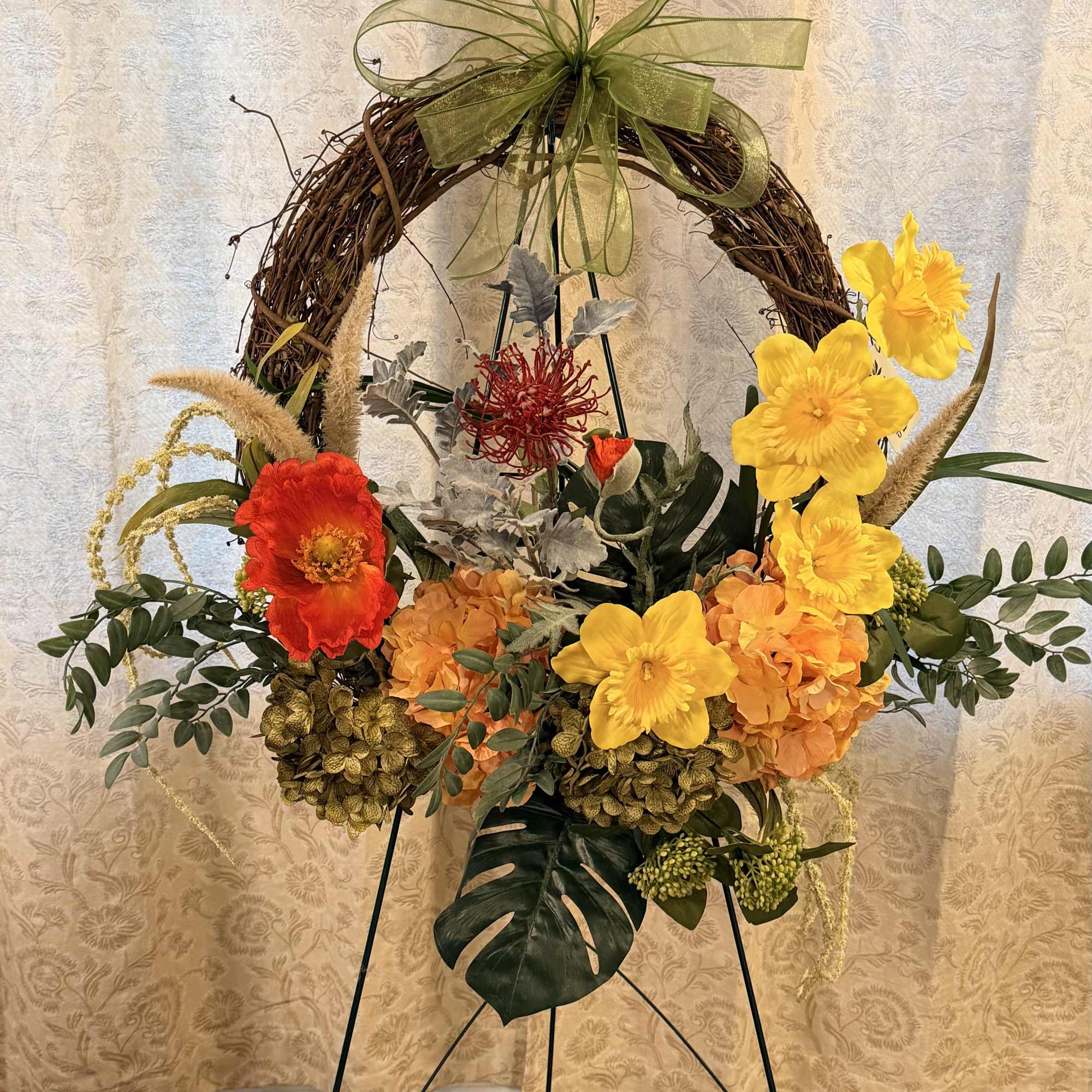 Floral wreath on a metal stand with yellow and orange flowers and a green bow