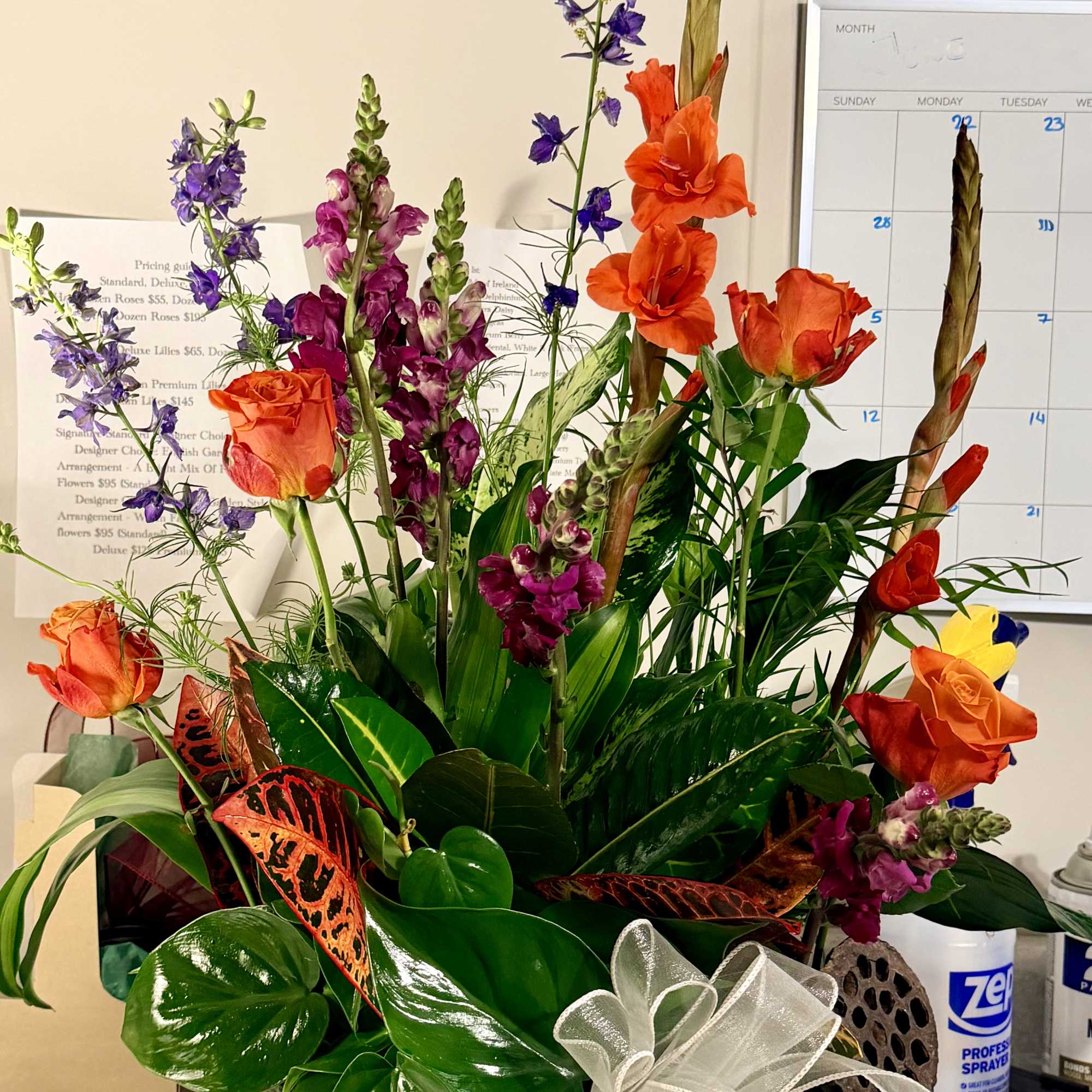 Tall mixed bouquet in a green bowl vase with orange roses and purple spikes