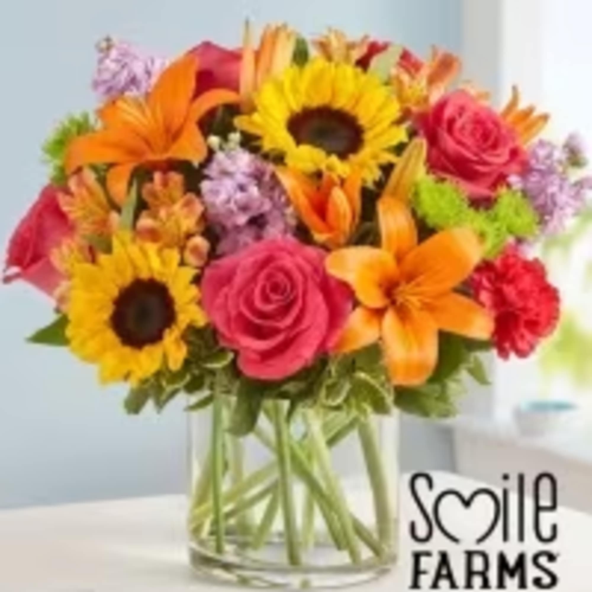 Mixed bouquet of sunflowers, roses, lilies, and carnations in a glass vase
