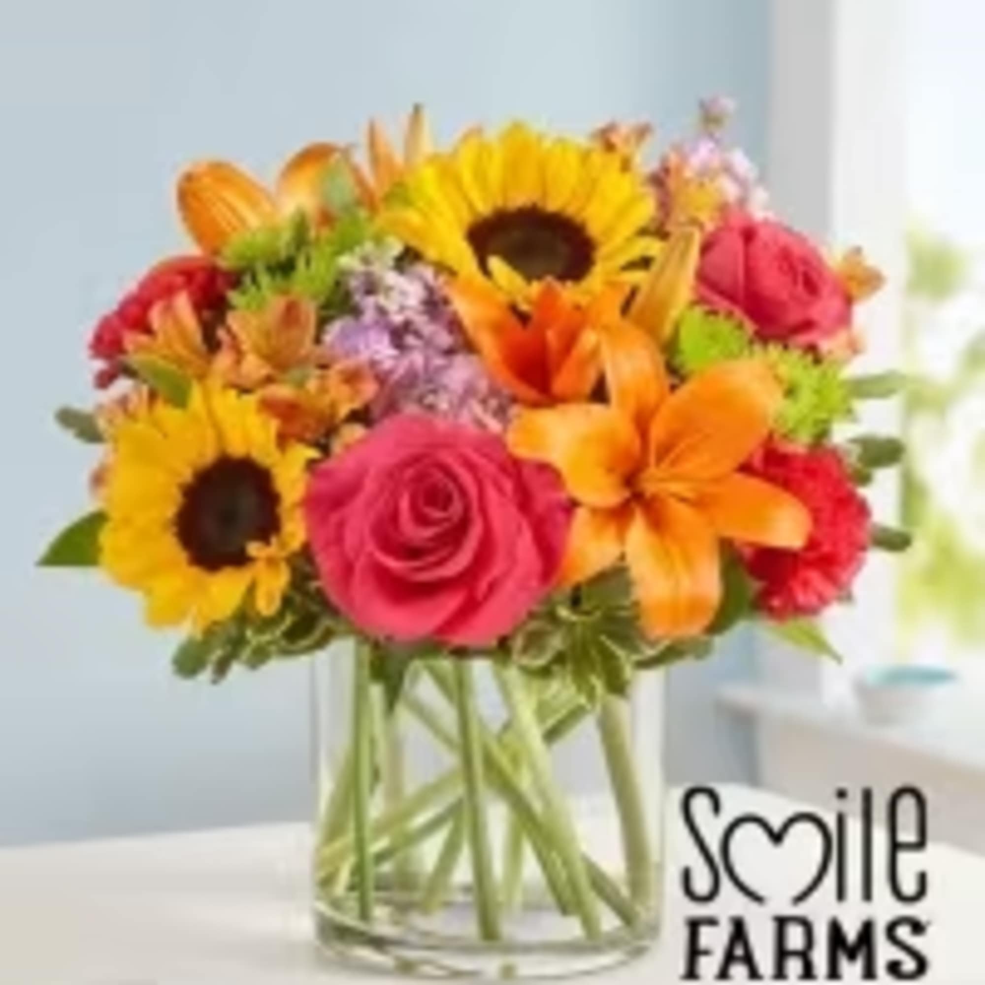 Bright mixed bouquet in a clear glass vase with sunflowers, roses, and lilies