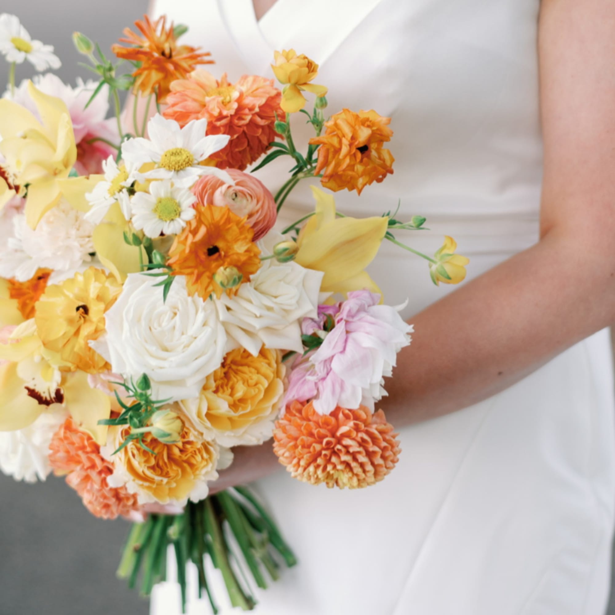 Bride holding a hand-tied bouquet of white roses, yellow calla lilies, and orange blooms