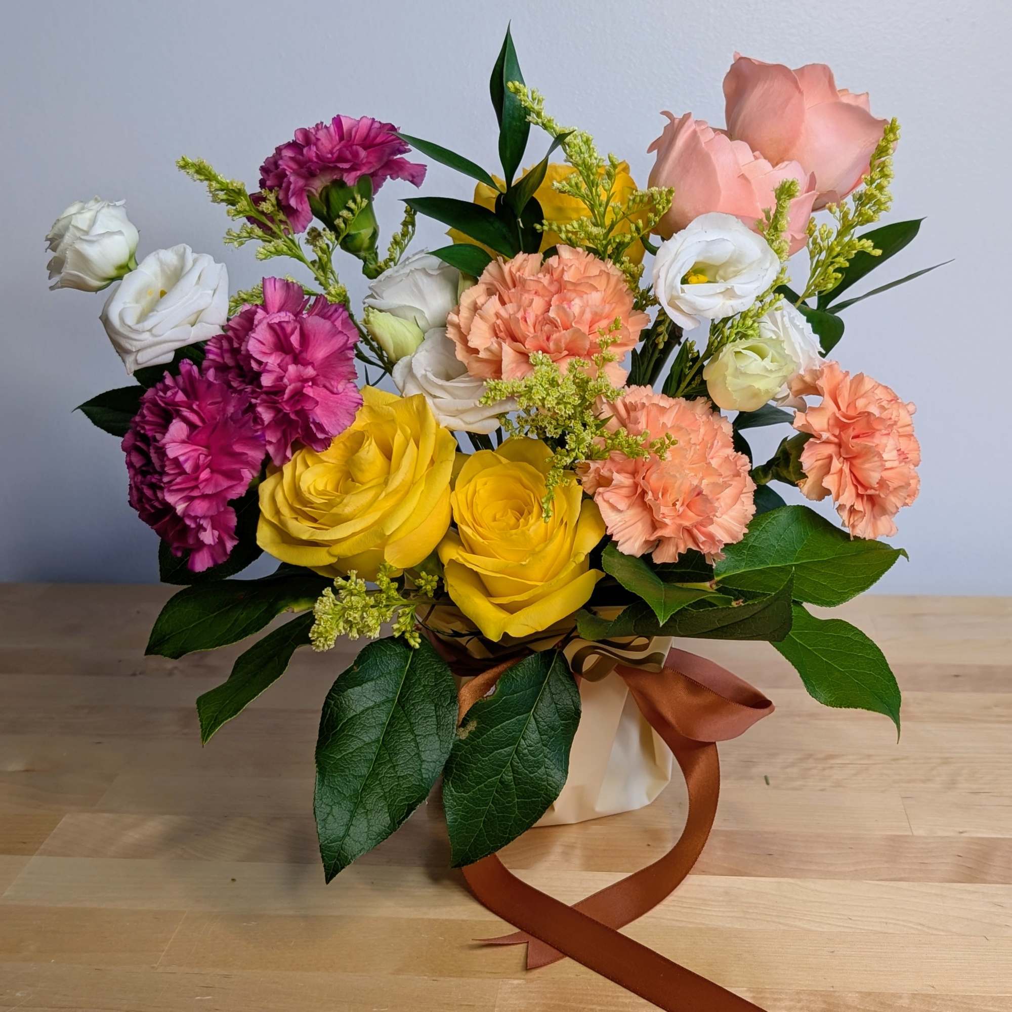 Bouquet of yellow roses, pink carnations, and white lisianthus in a wrapped vase