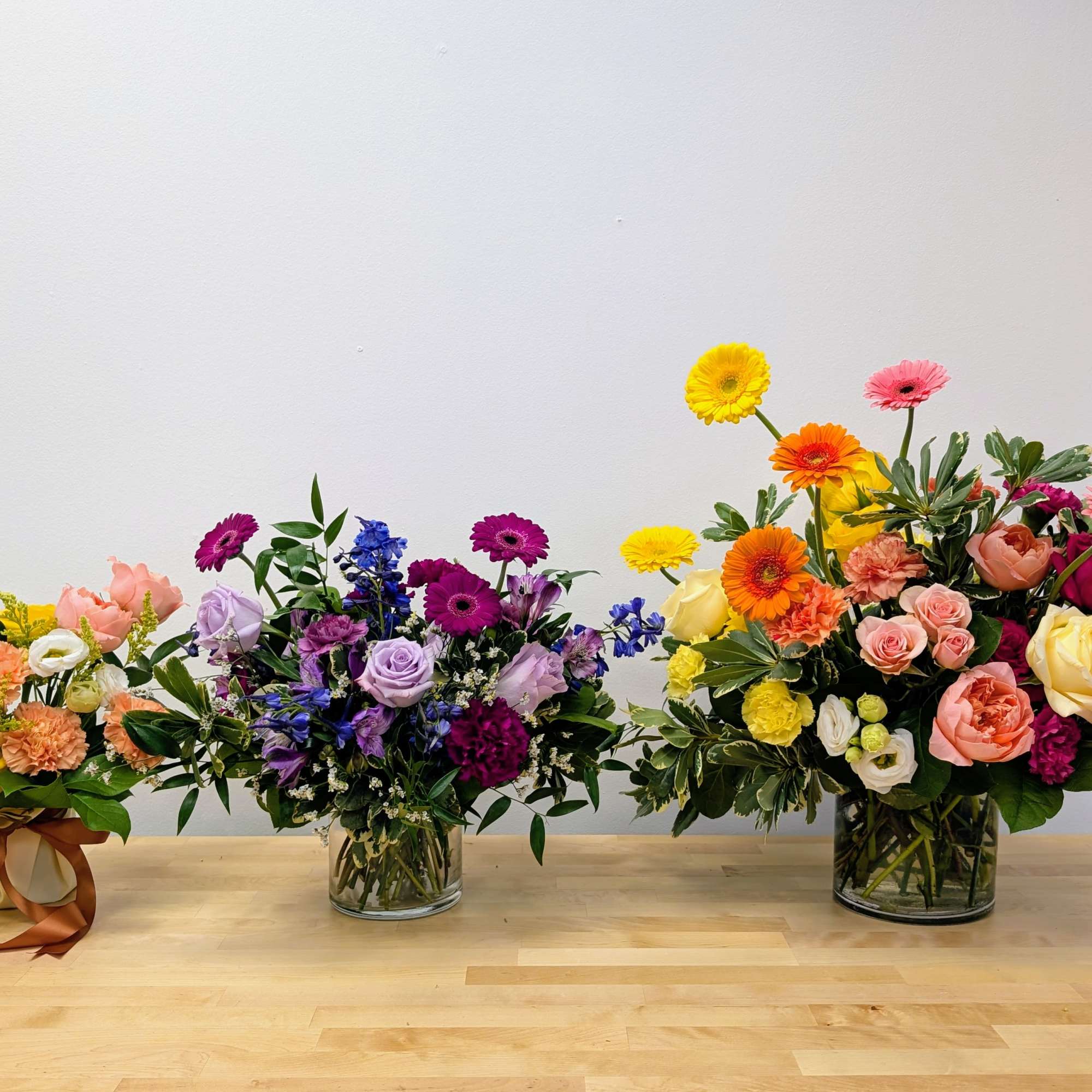 Three colorful flower arrangements in glass vases on a wooden table