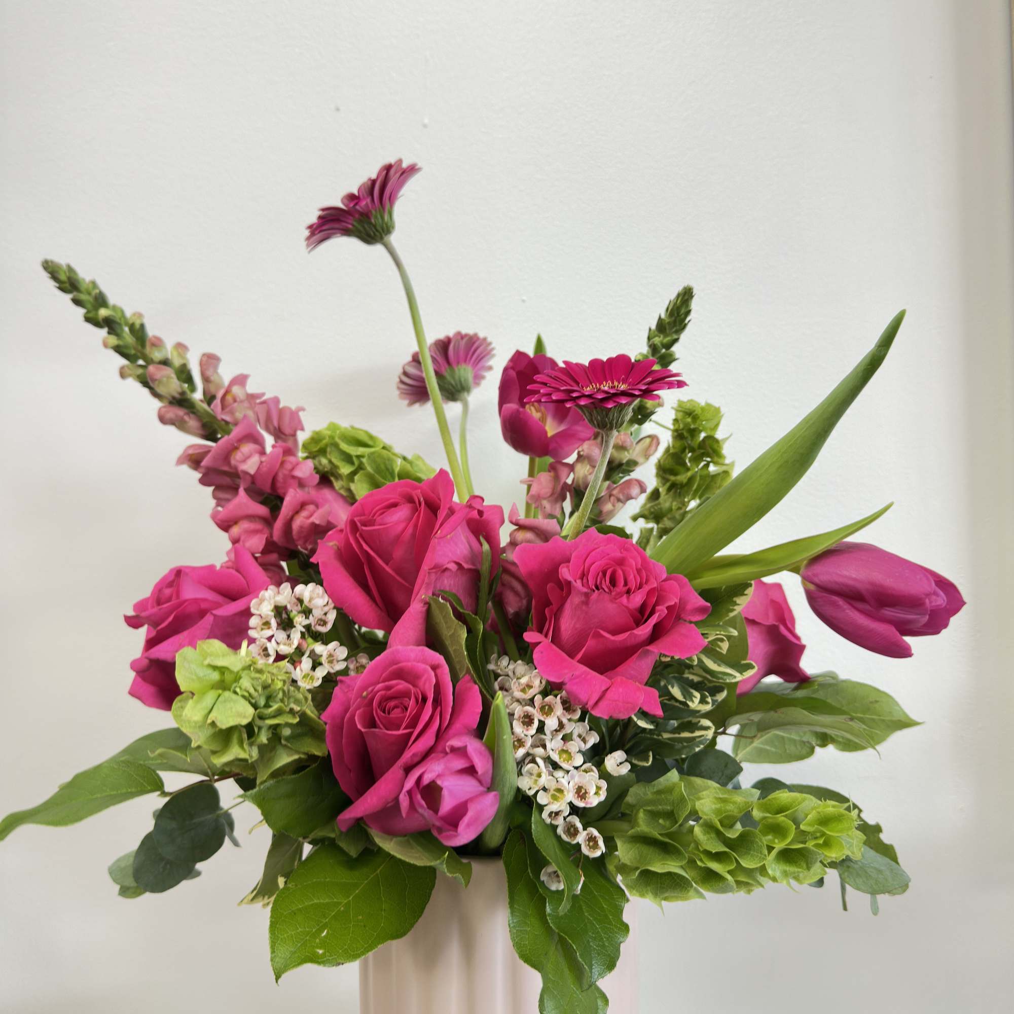 Pink roses and mixed blooms arranged in a pale vase.