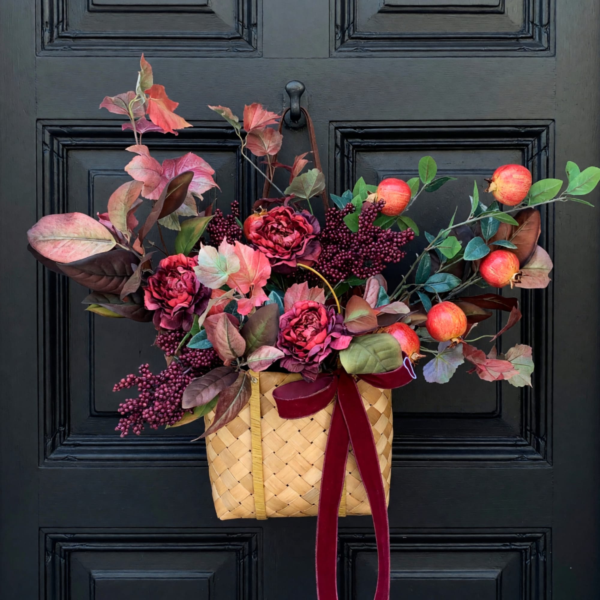 Autumn floral basket with burgundy flowers, berries, and apples on a black door.