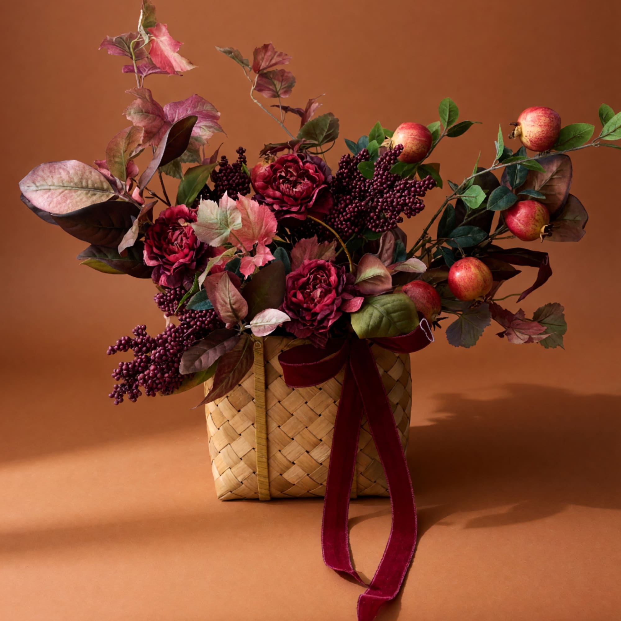 Autumn floral arrangement in a woven basket with burgundy flowers and apples