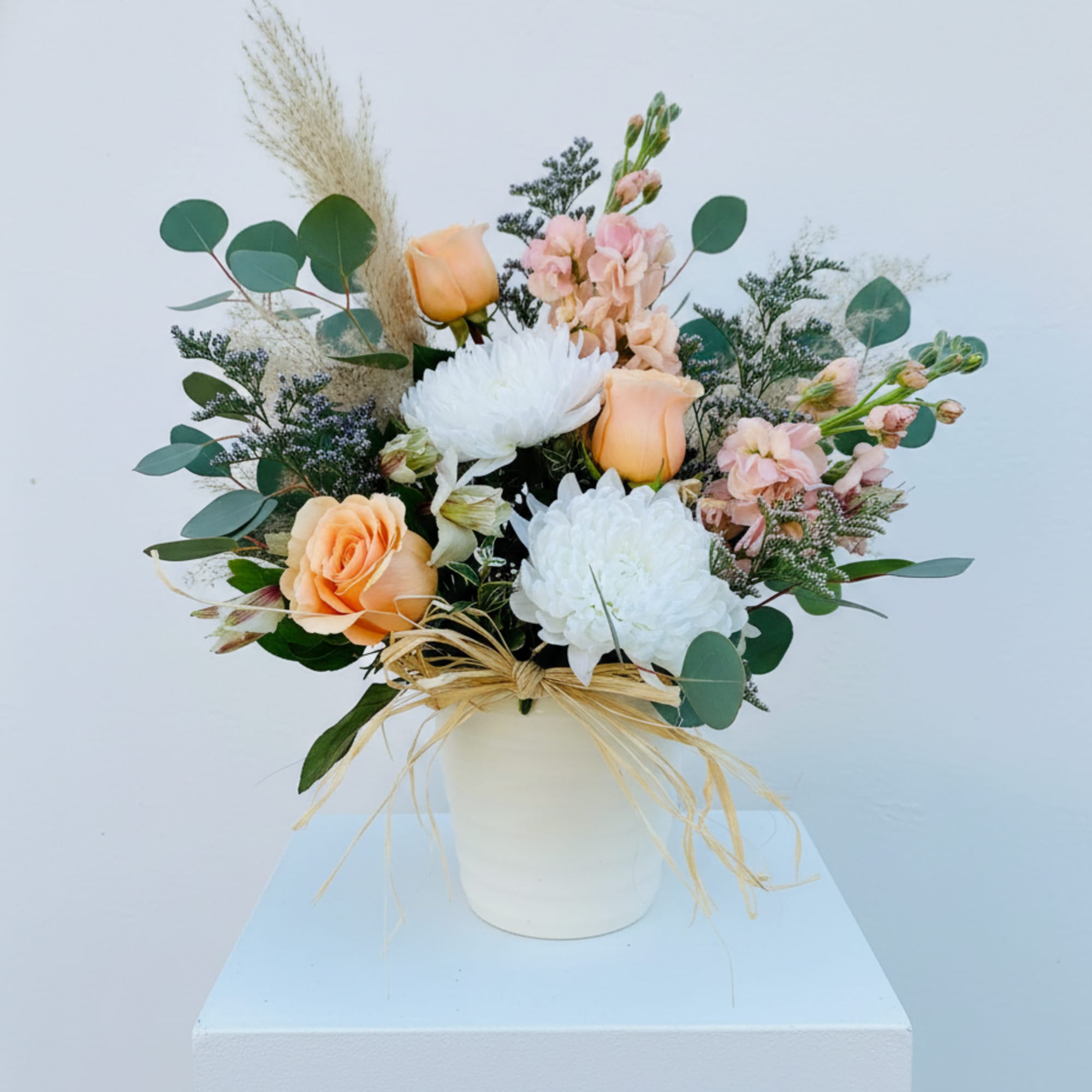 Peach and white floral arrangement in a white vase with eucalyptus