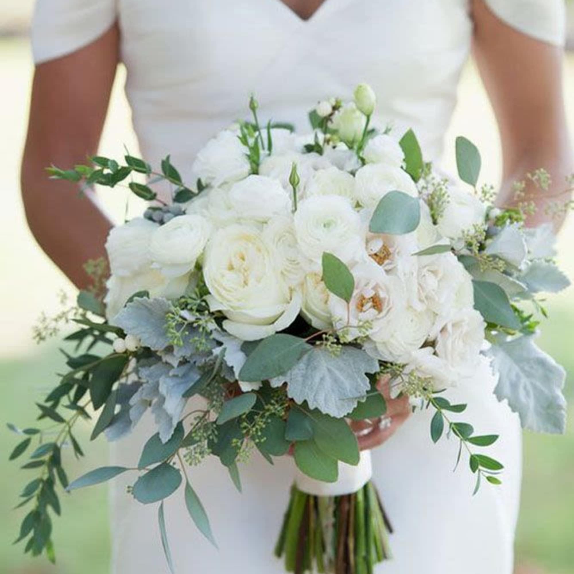 A classic and elegant bridal bouquet featuring lush white roses, soft ranunculus