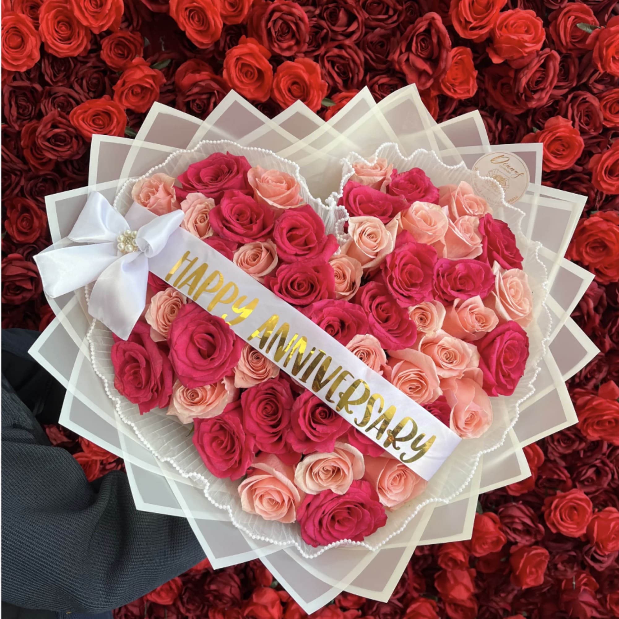 Heart-shaped bouquet of pink and peach roses with a Happy Anniversary sash