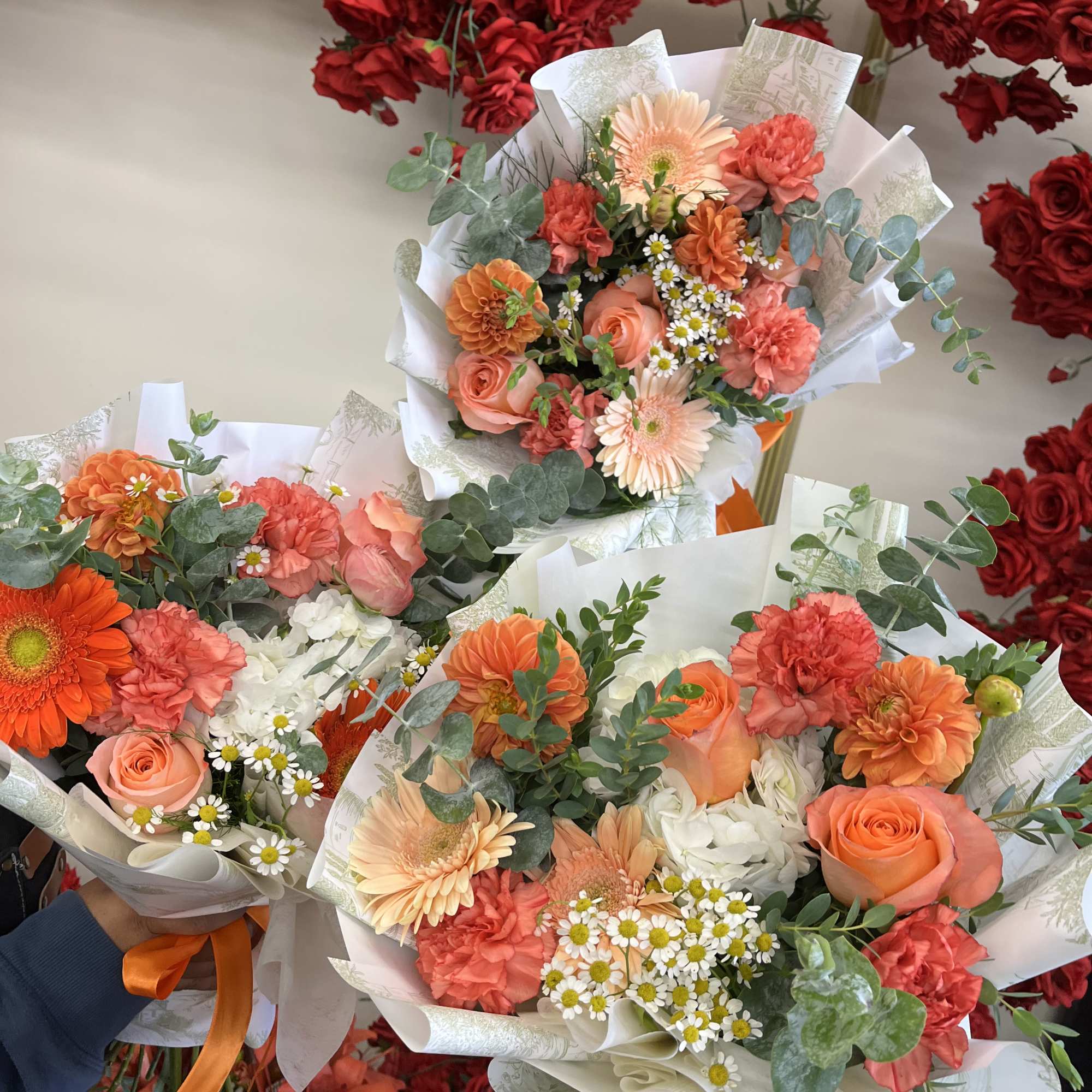 Three mixed bouquets with peach, coral, and white flowers wrapped in white paper