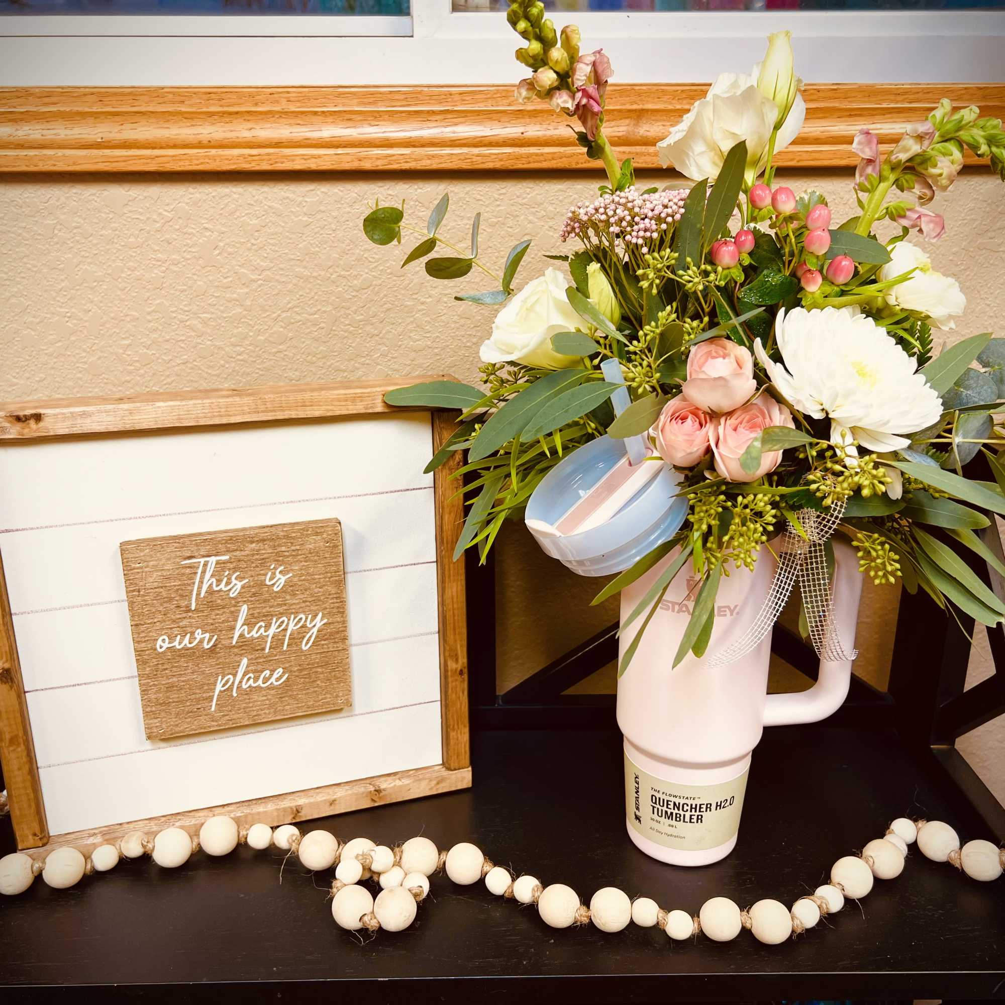 Mixed bouquet in a pink tumbler beside a framed sign