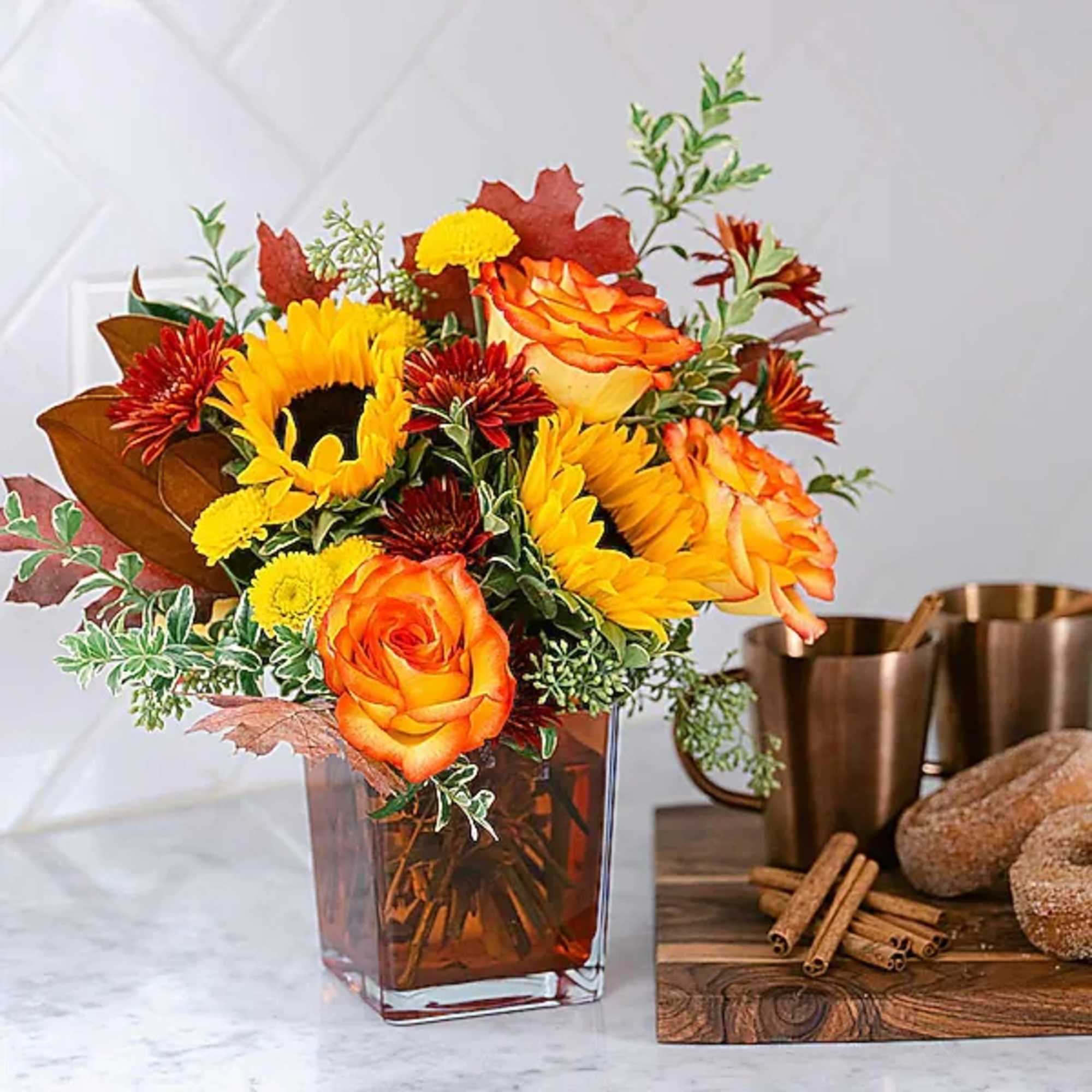 Orange roses and sunflowers arranged in a square glass vase