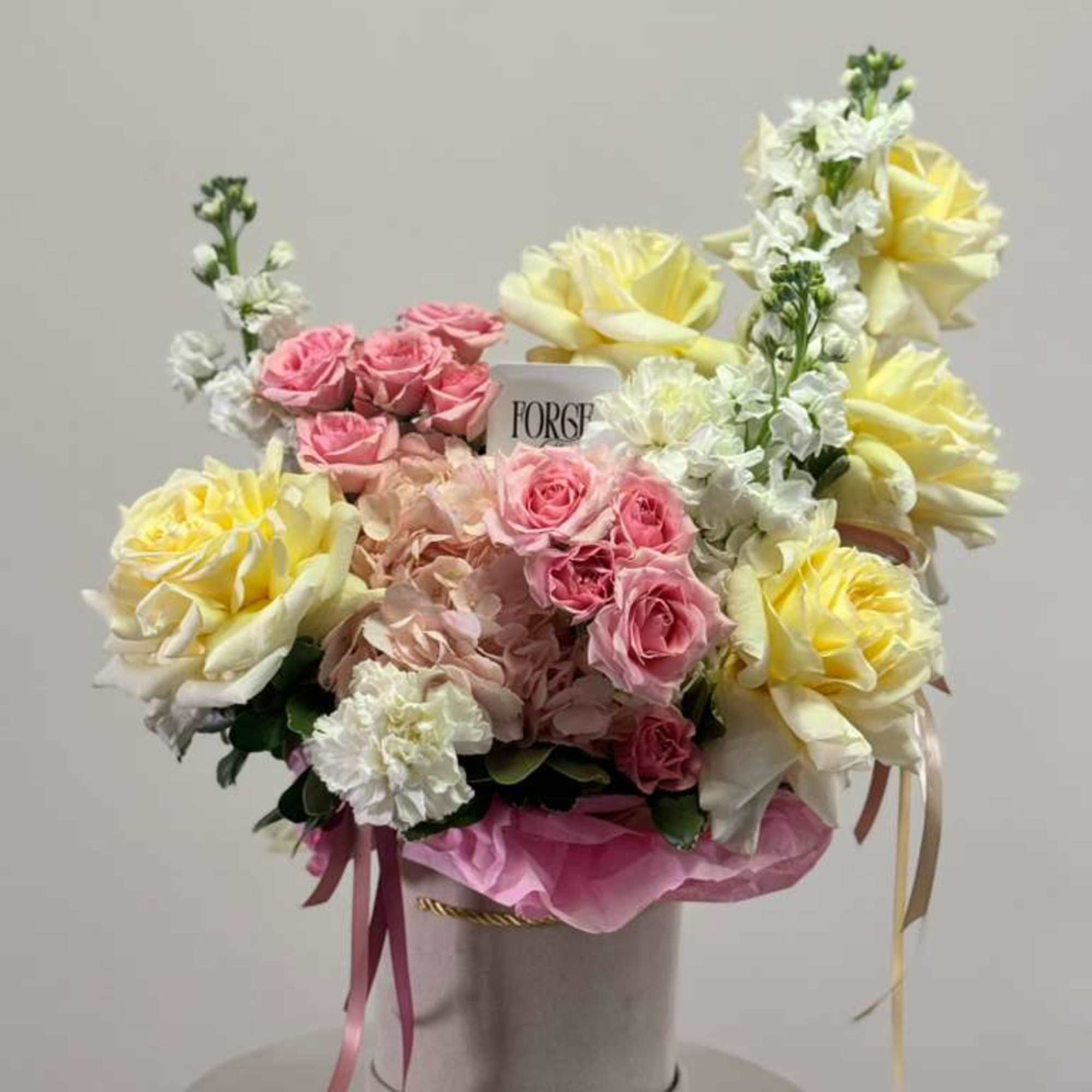 Pink and yellow roses arranged in a round hatbox with ribbons
