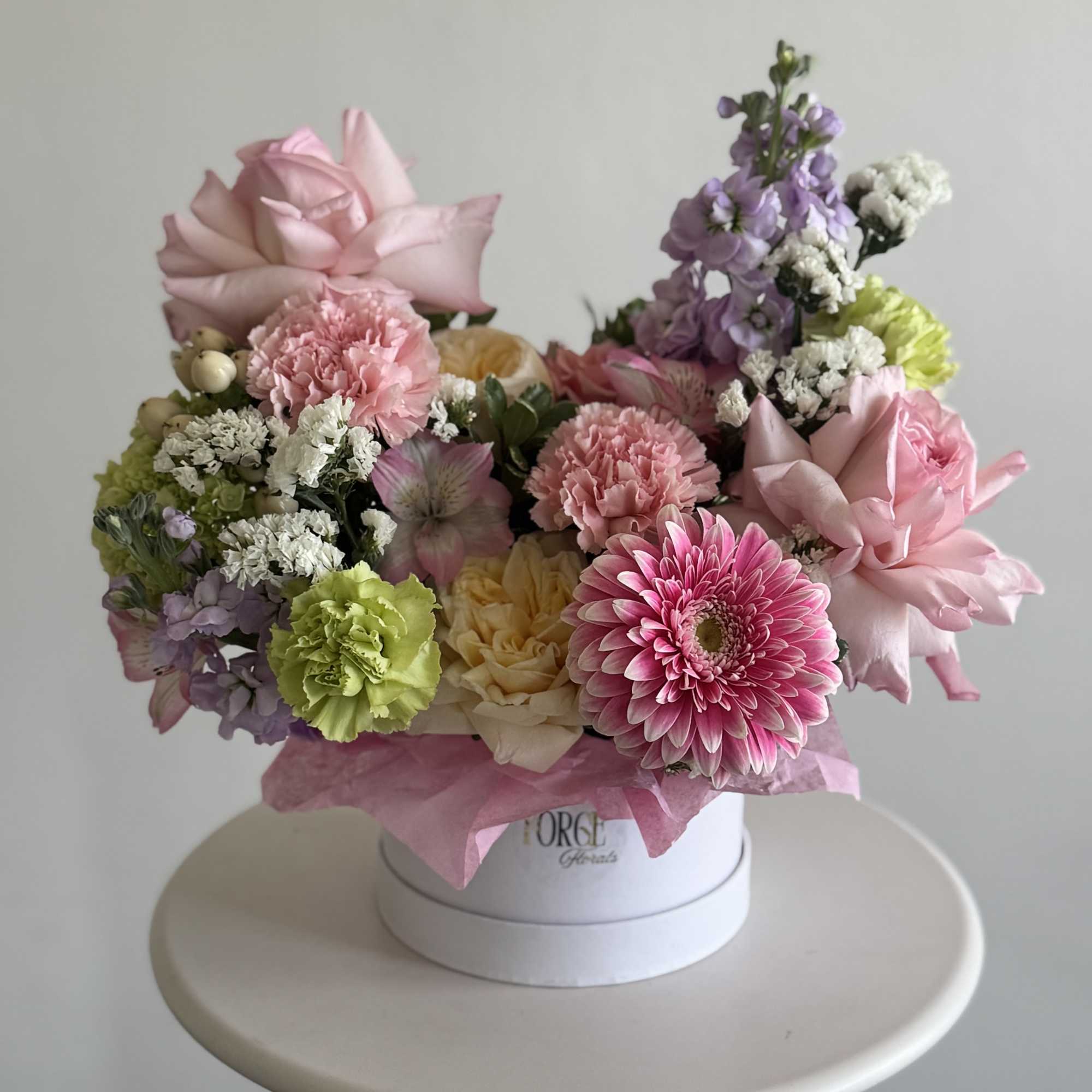 Pink and lavender mixed flower arrangement in a white hat box