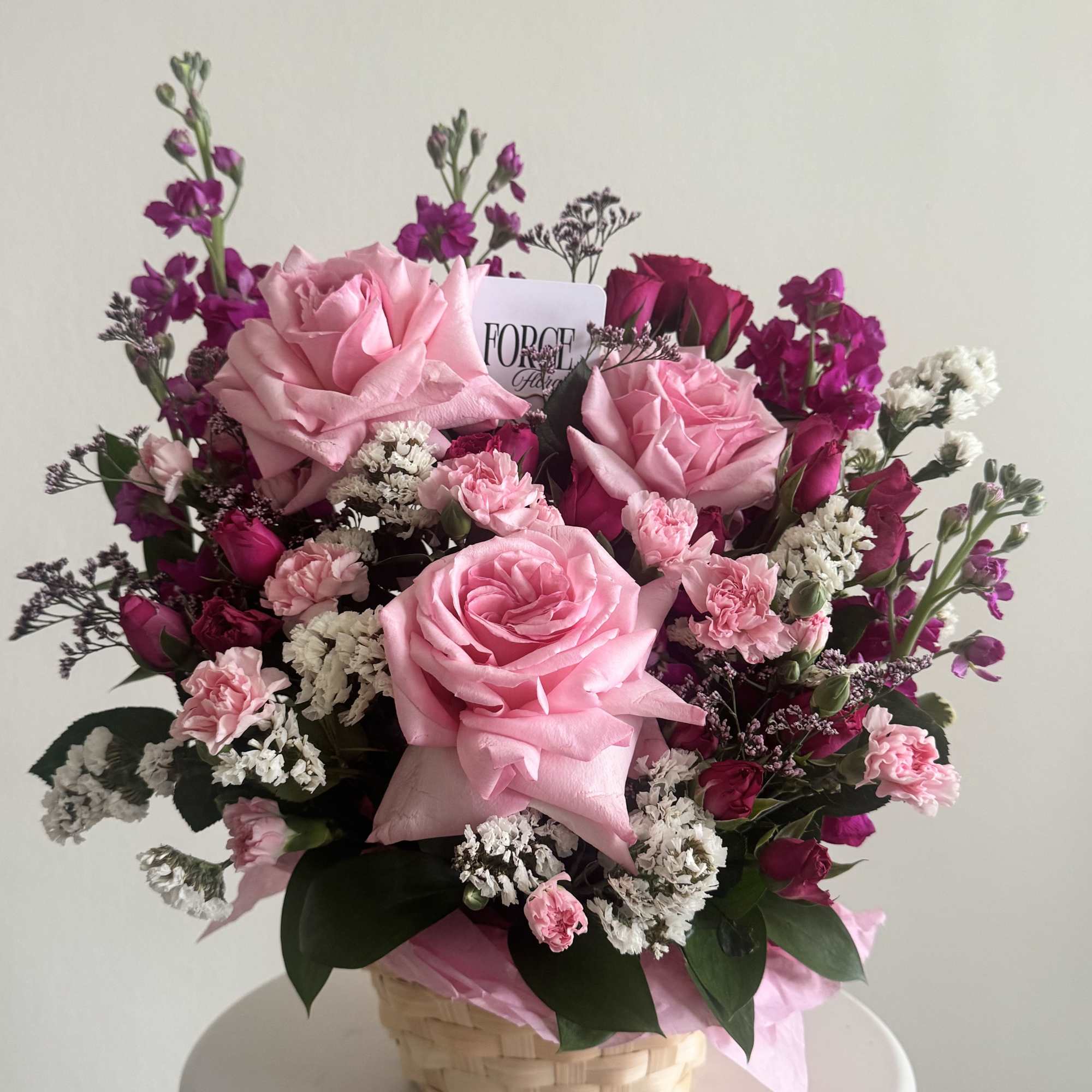 Pink roses and carnations arranged in a basket with white filler flowers
