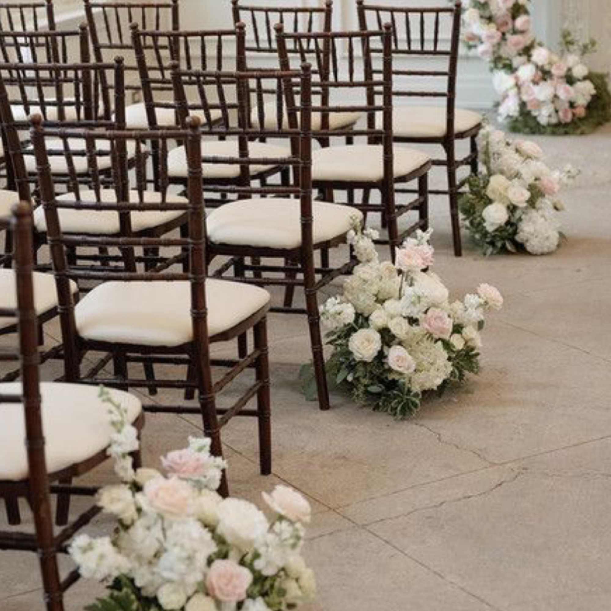 Pastel floral arrangements line rows of chairs in a ceremony space.
