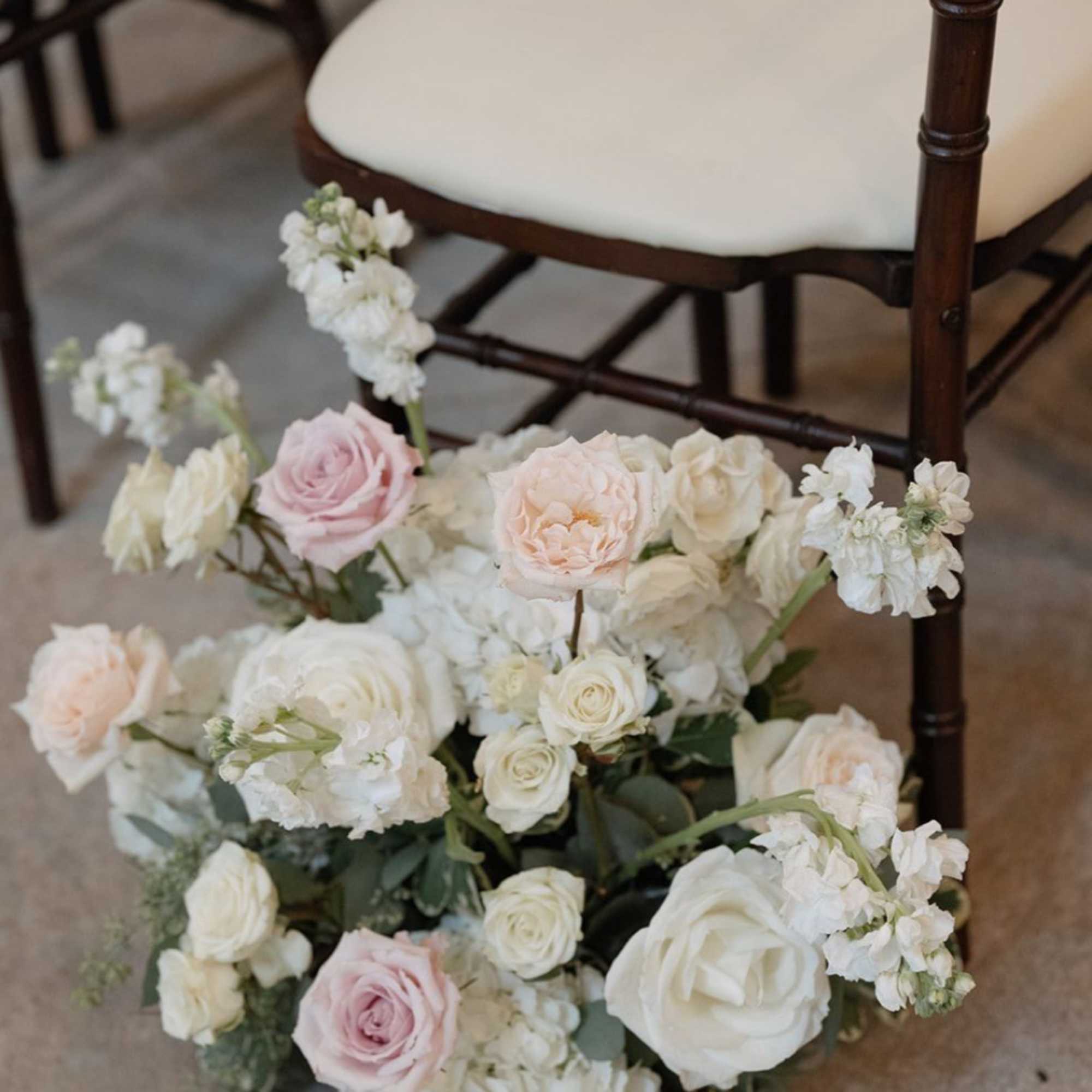 Wedding floral arrangement with white and blush roses on the floor beside a chair