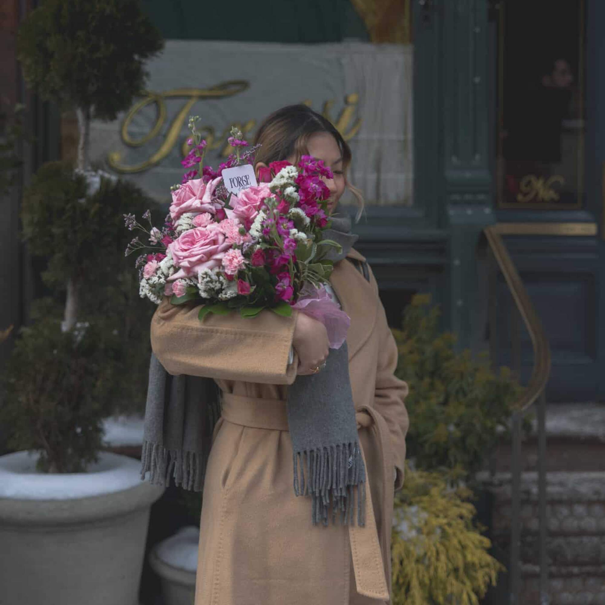 Woman holding a pink bouquet wrapped in tan paper outdoors