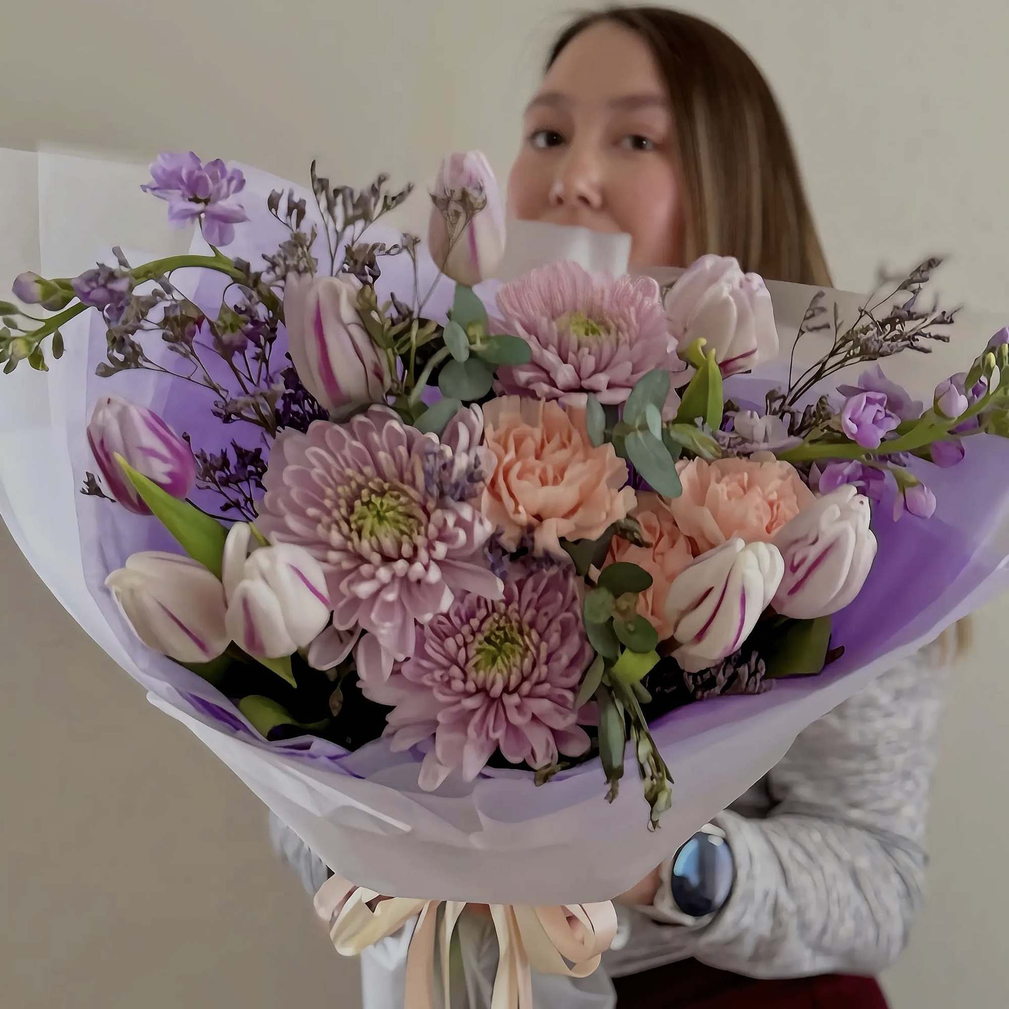 Woman holding a pastel bouquet of tulips and chrysanthemums wrapped in lavender paper