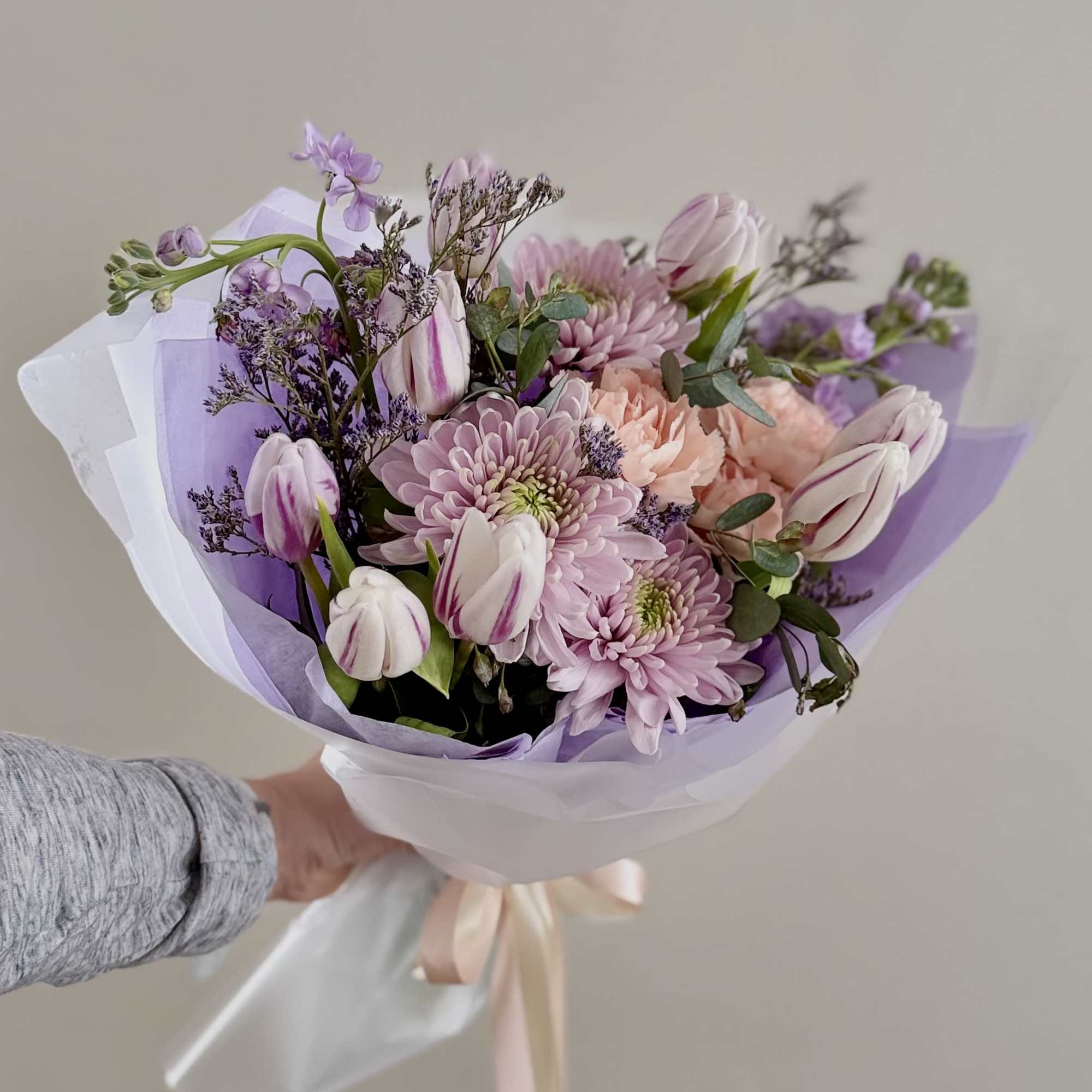 Handheld bouquet of pink and lavender flowers wrapped in white and purple paper
