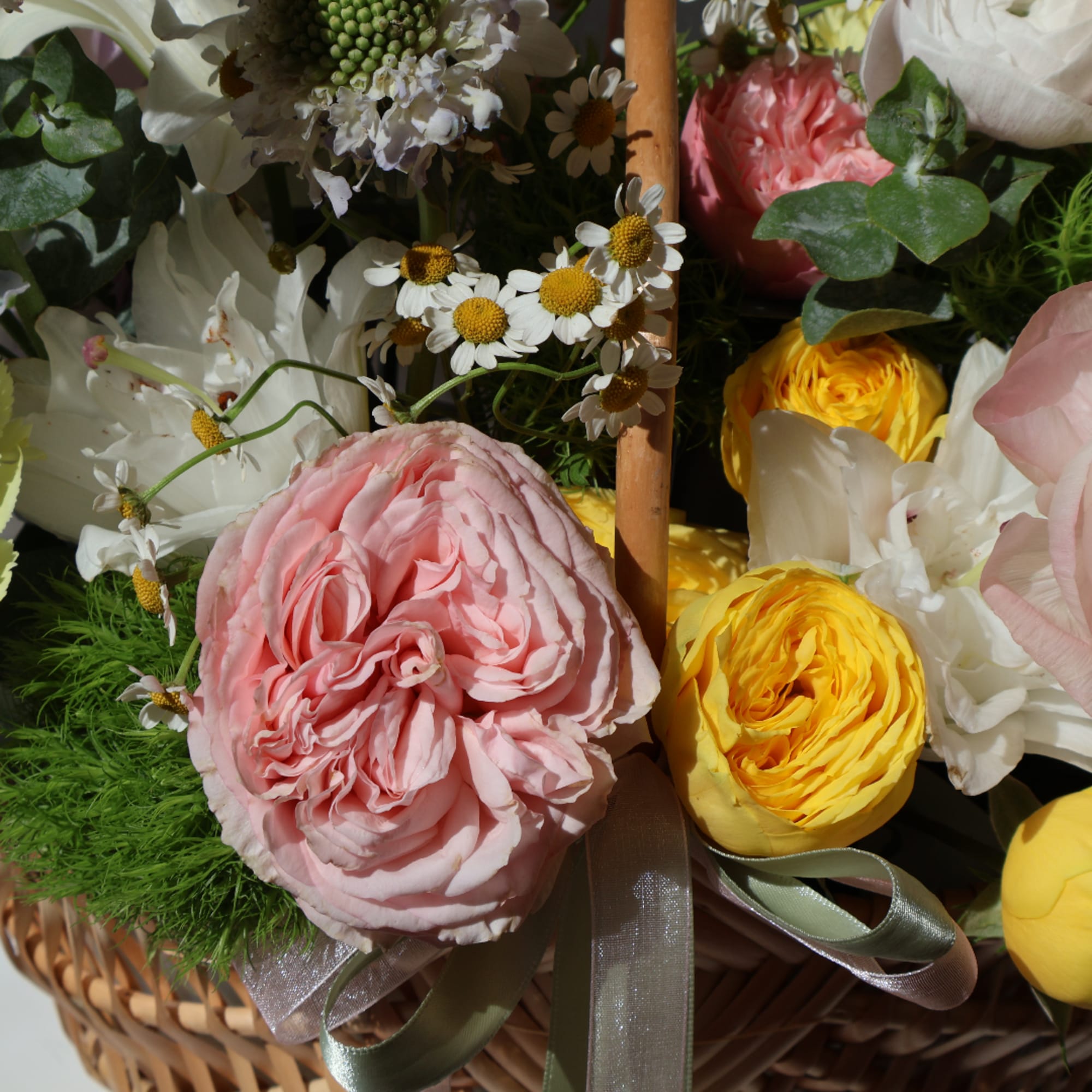 Basket of pink, yellow, and white flowers with ribbon accents