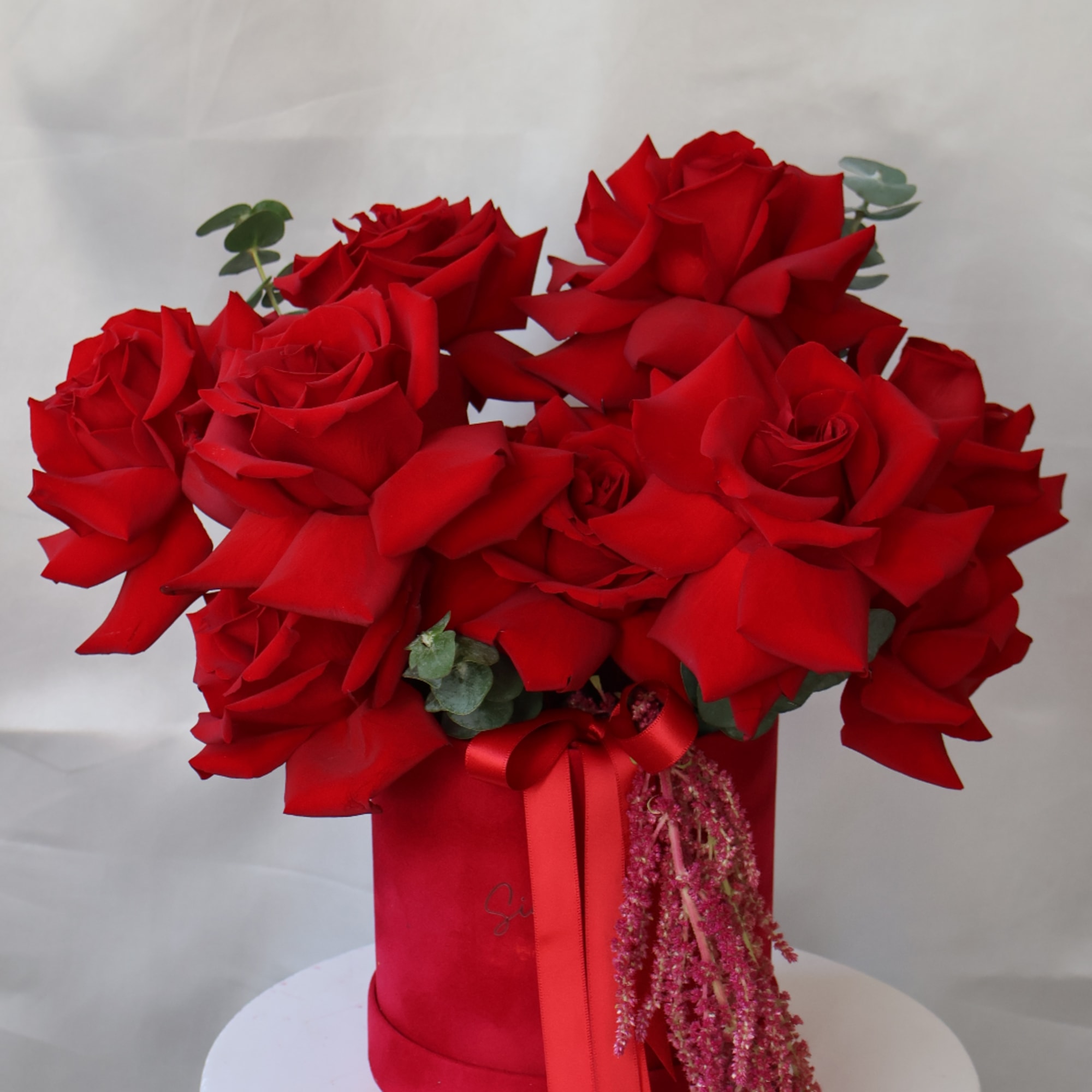 Red roses arranged in a red box with a ribbon bow