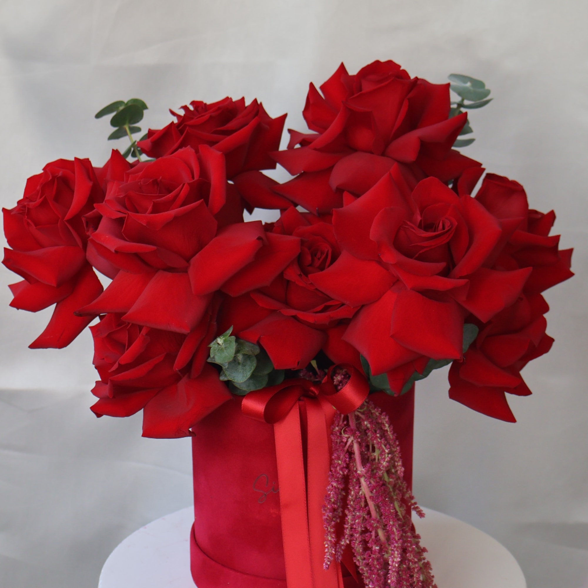Red roses arranged in a tall red box with a ribbon.