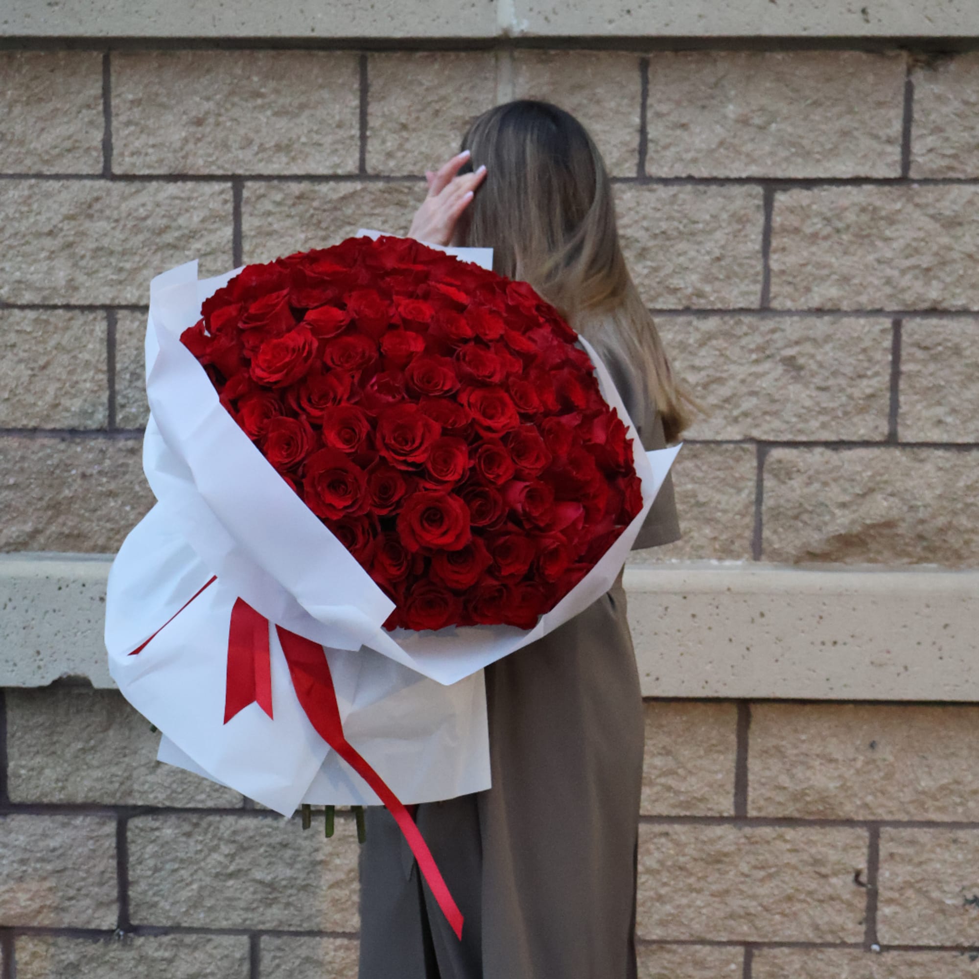 Large bouquet of red roses wrapped in white paper with a red ribbon