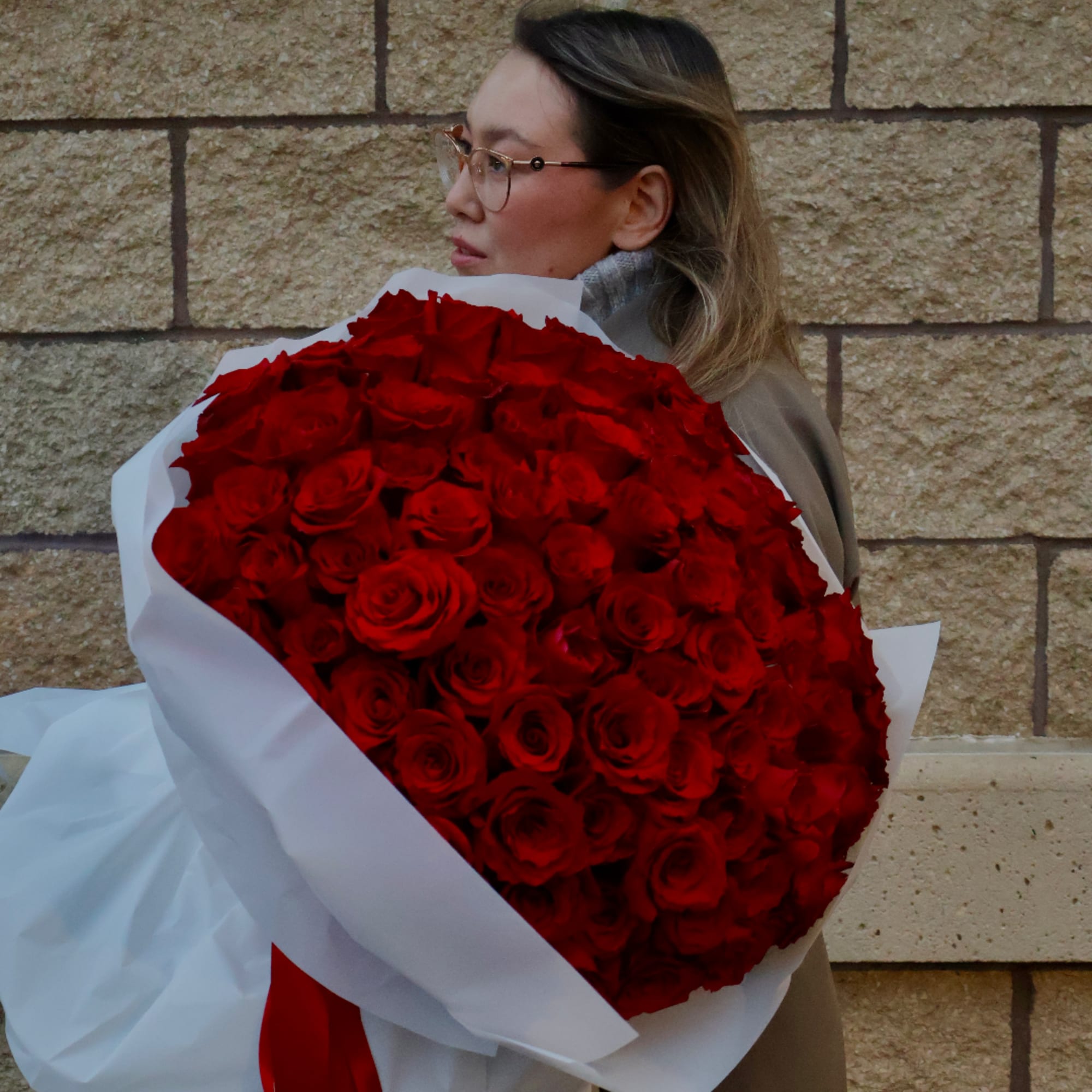 Woman holding a large bouquet of red roses wrapped in white paper
