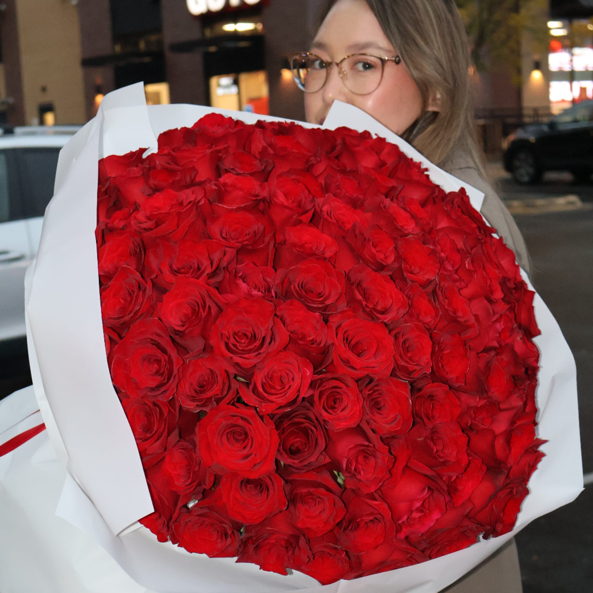 Woman holding a large bouquet of red roses wrapped in white paper, photo 3 of 5