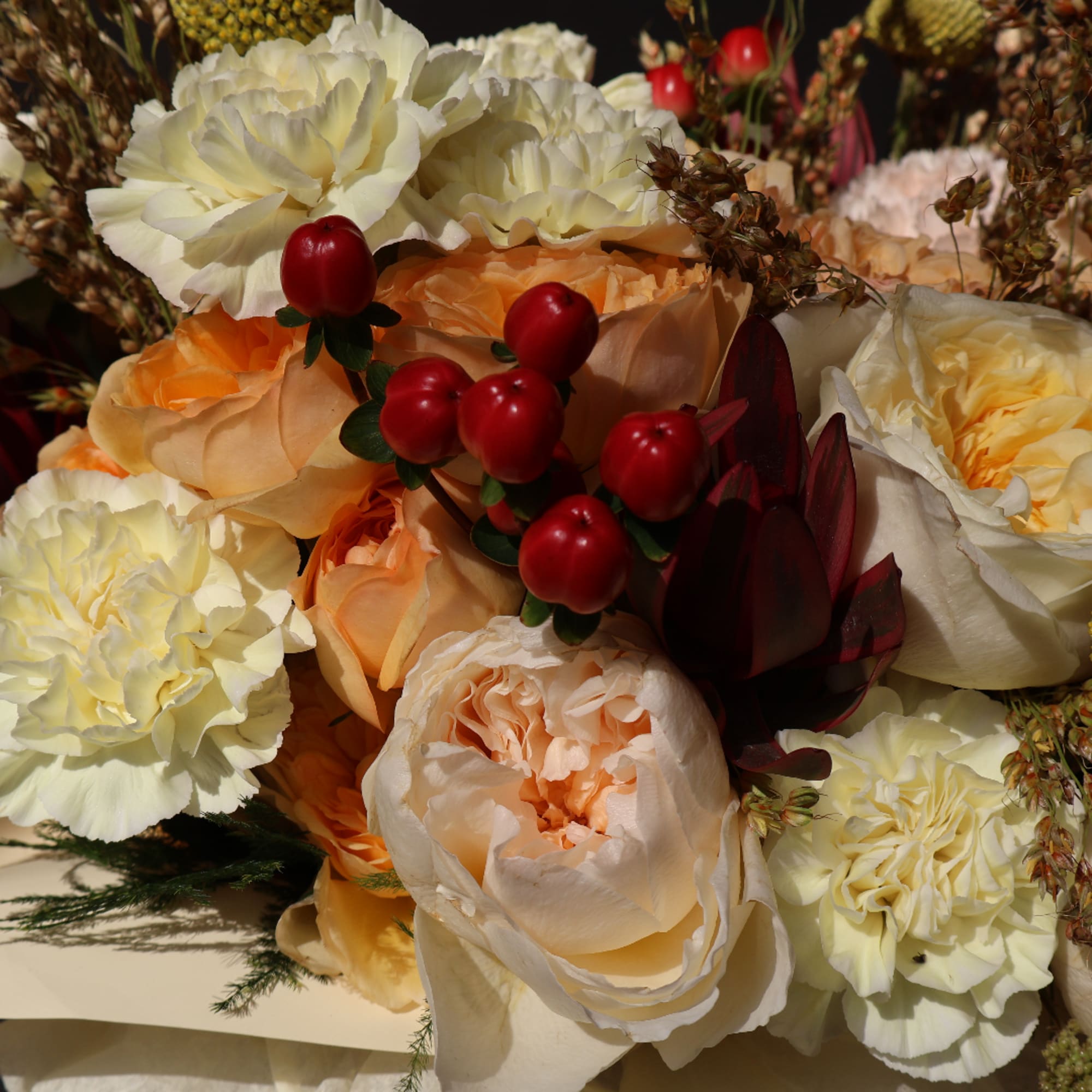 Bouquet of cream and peach roses with white carnations and red berries