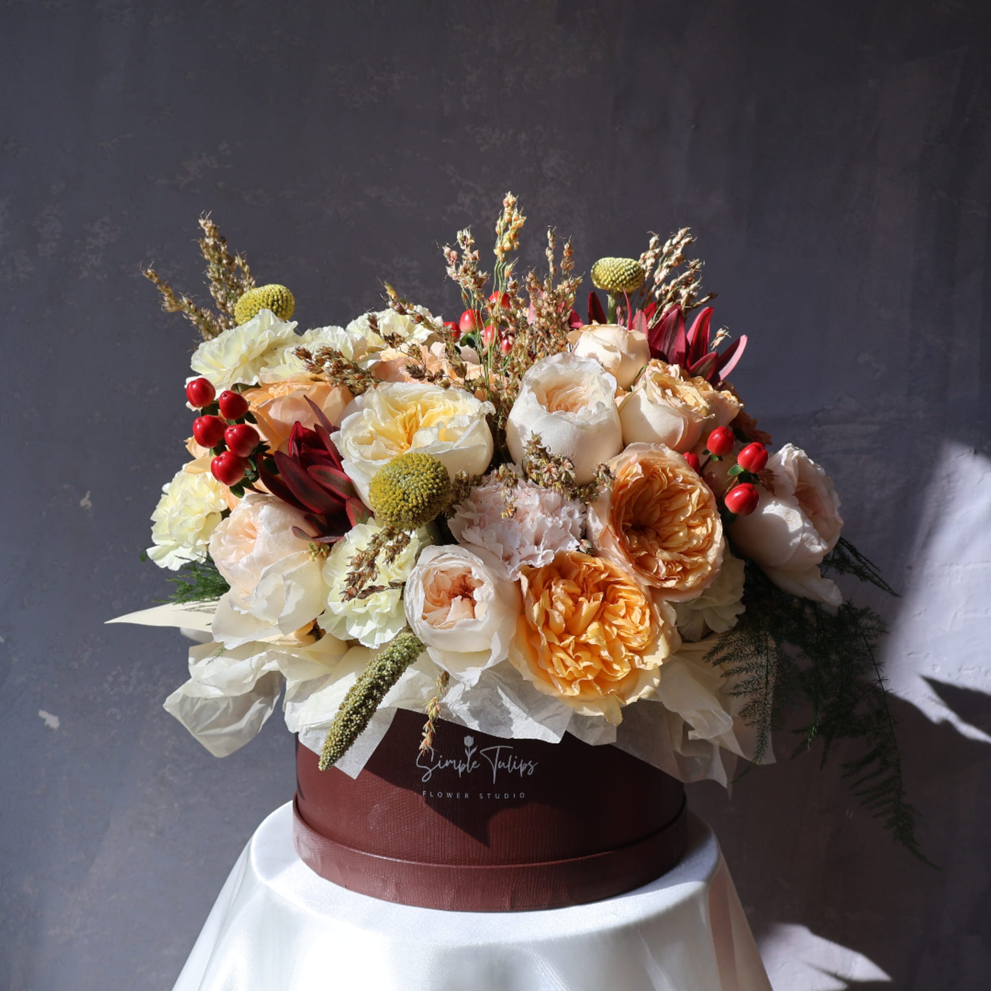 Mixed bouquet of cream, peach, and burgundy flowers in a round box