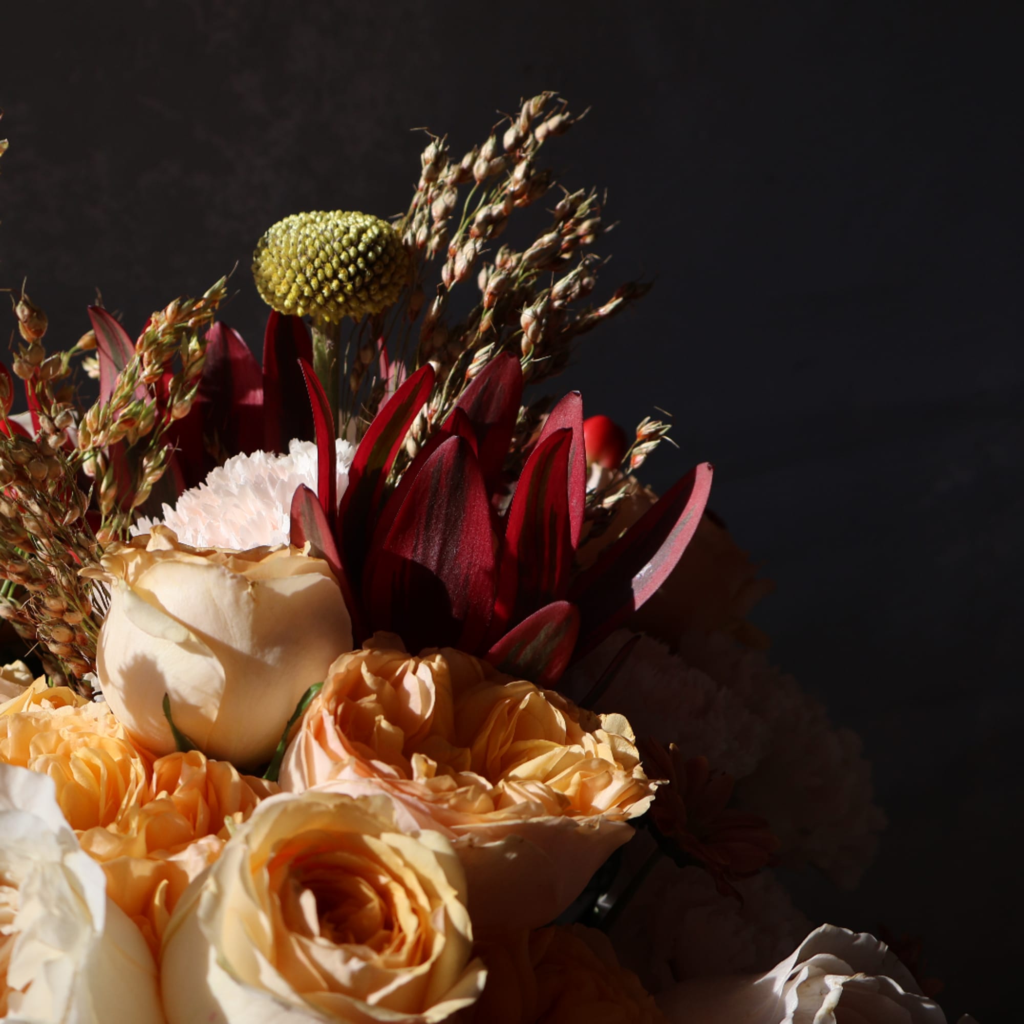 Bouquet of peach and cream roses with burgundy blooms against a dark background