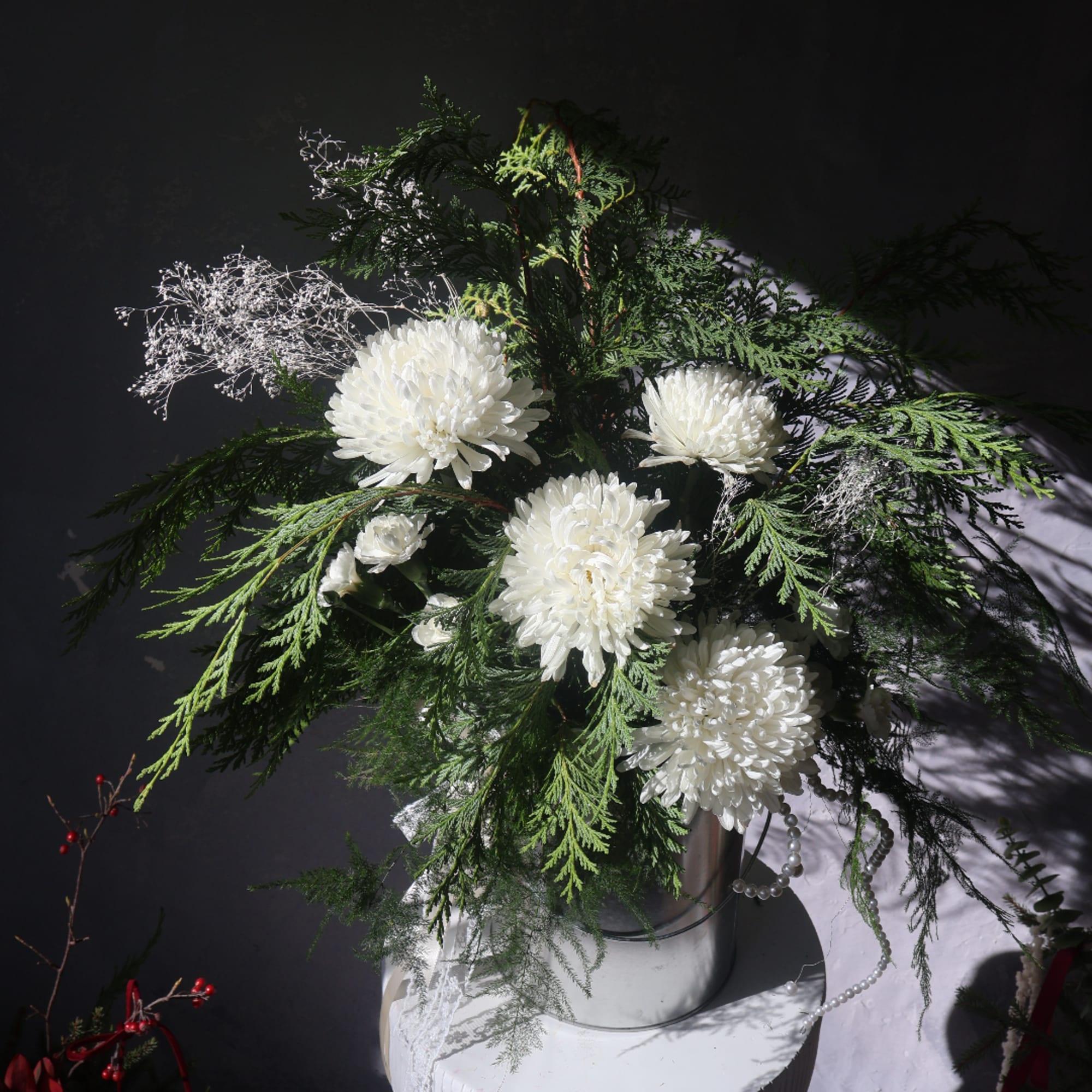 White chrysanthemum arrangement in a silver vase with evergreen foliage