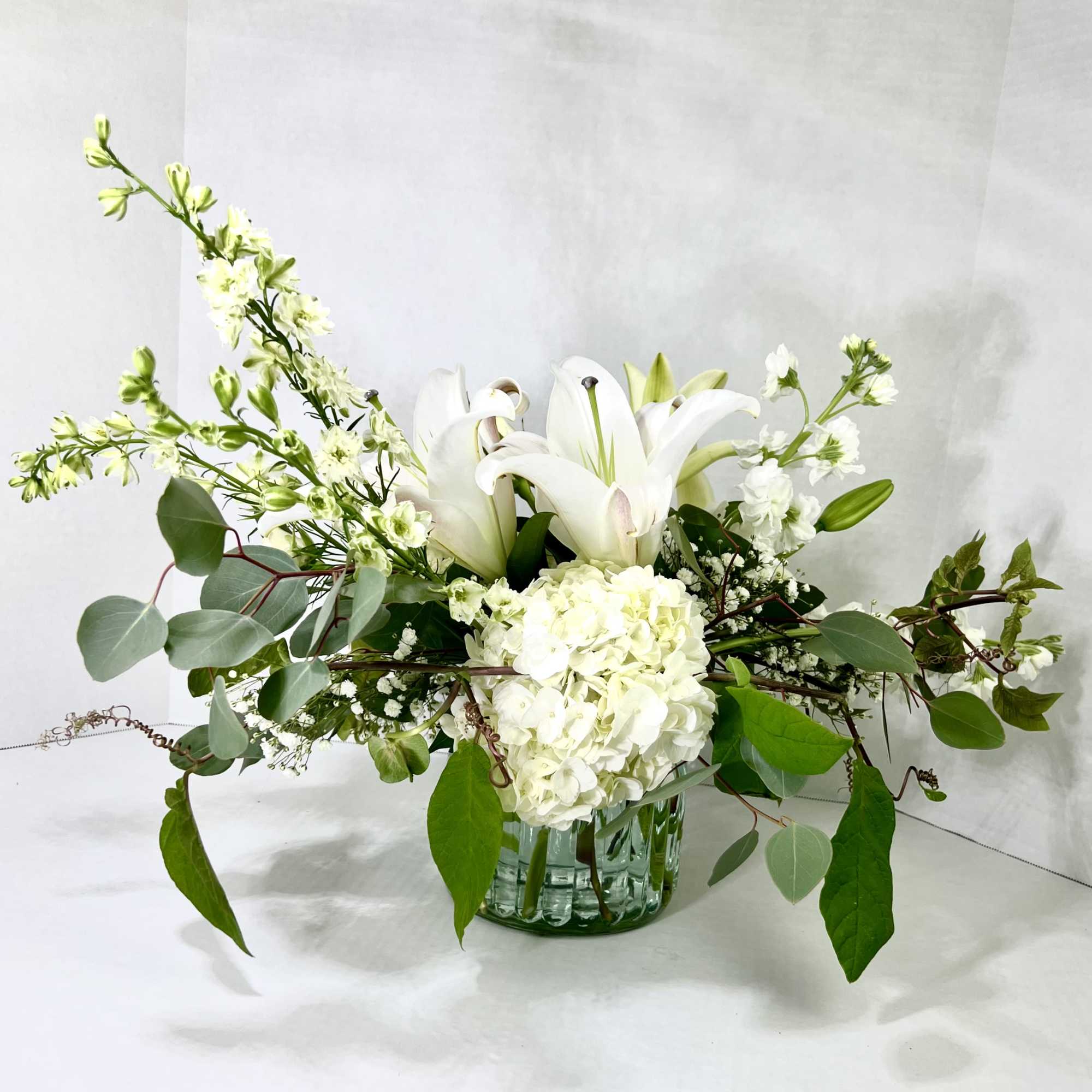 White lilies and hydrangea in a glass vase with airy greenery