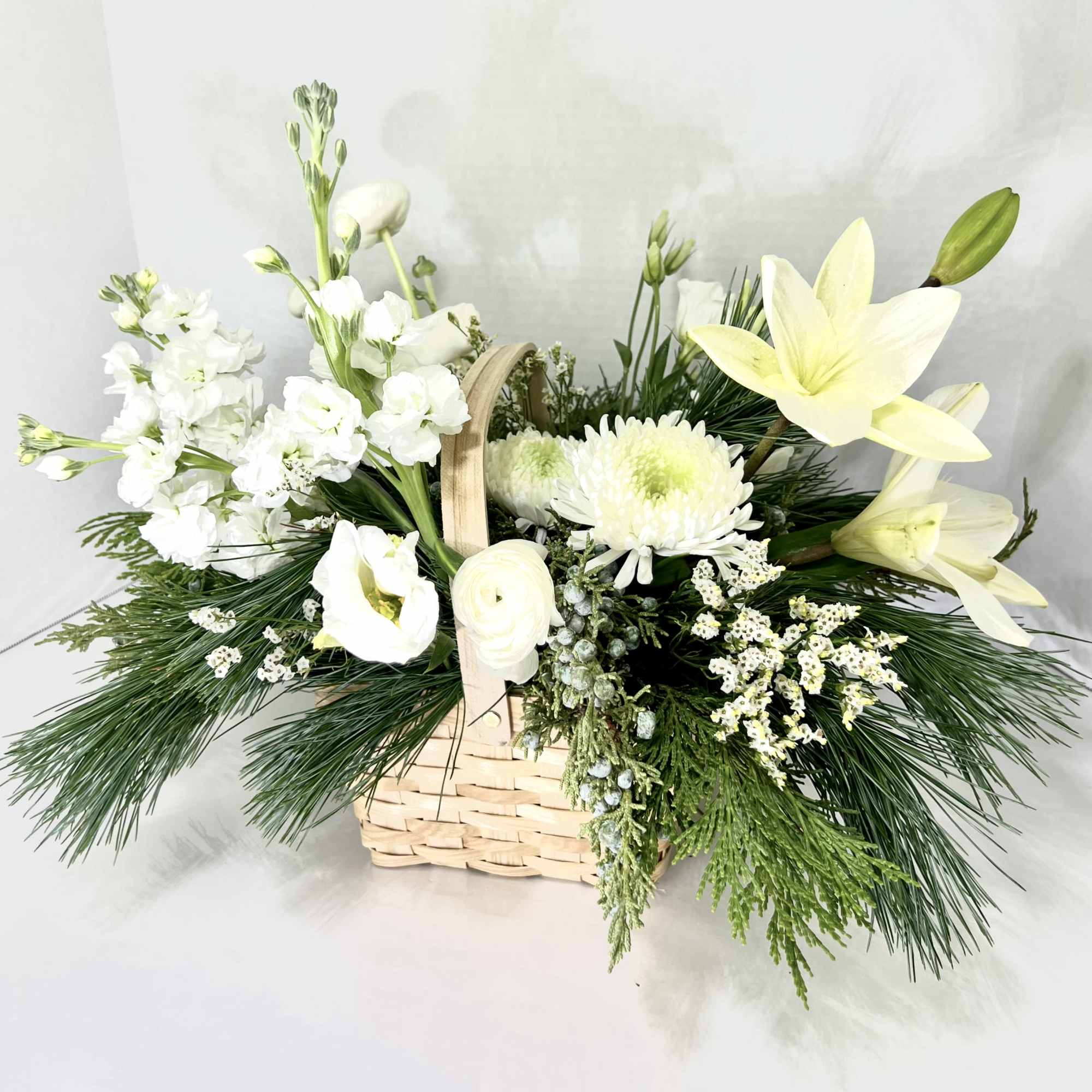 White flowers arranged in a wicker basket with pine greenery