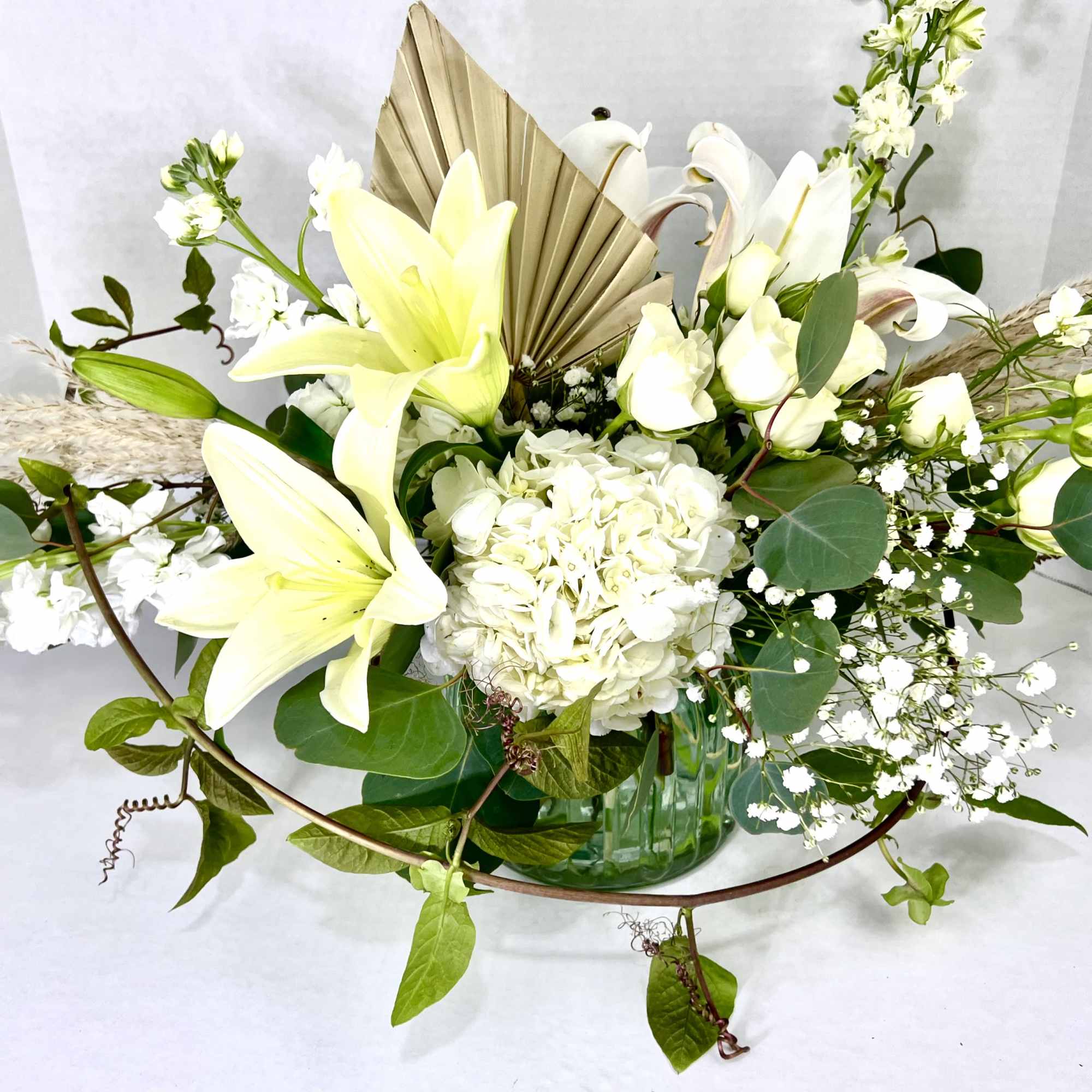 White lilies and hydrangea in a green glass vase with a fan accent