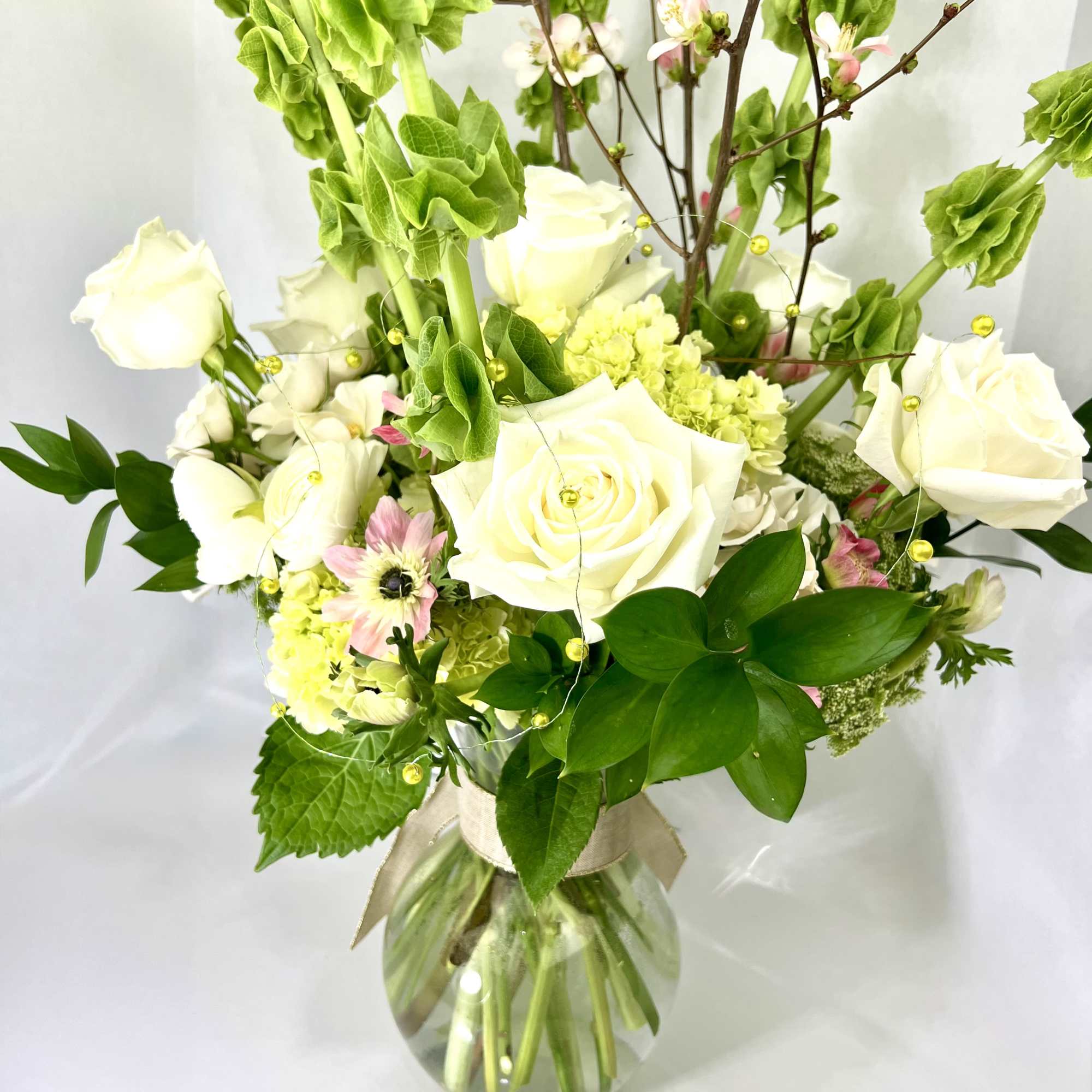 White roses and pink blossoms in a glass vase with tall green stems