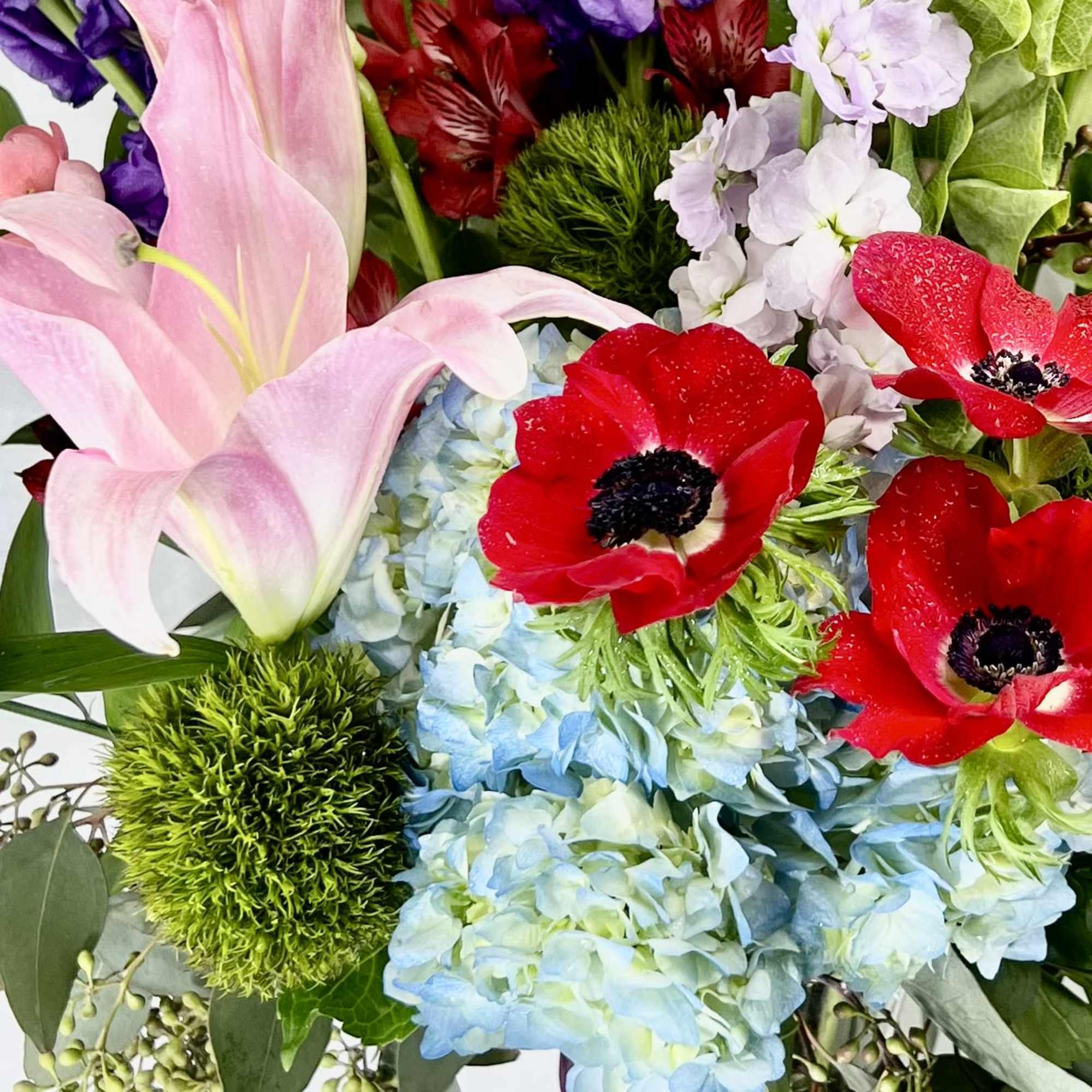 Pink lilies, red anemones, and blue hydrangeas in a mixed bouquet