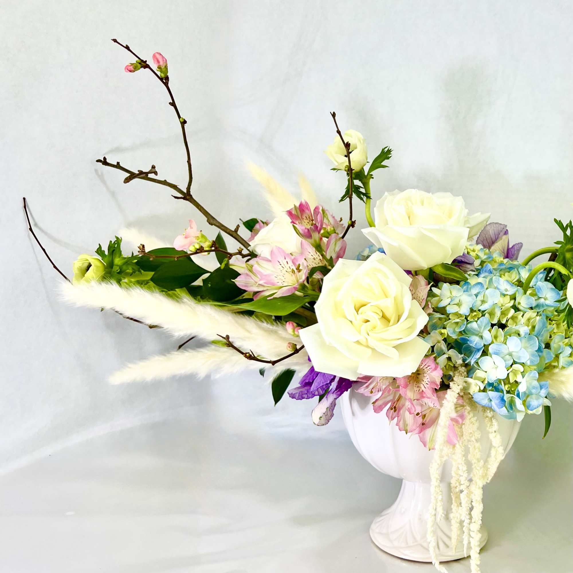 White roses and blue hydrangeas in a white pedestal vase