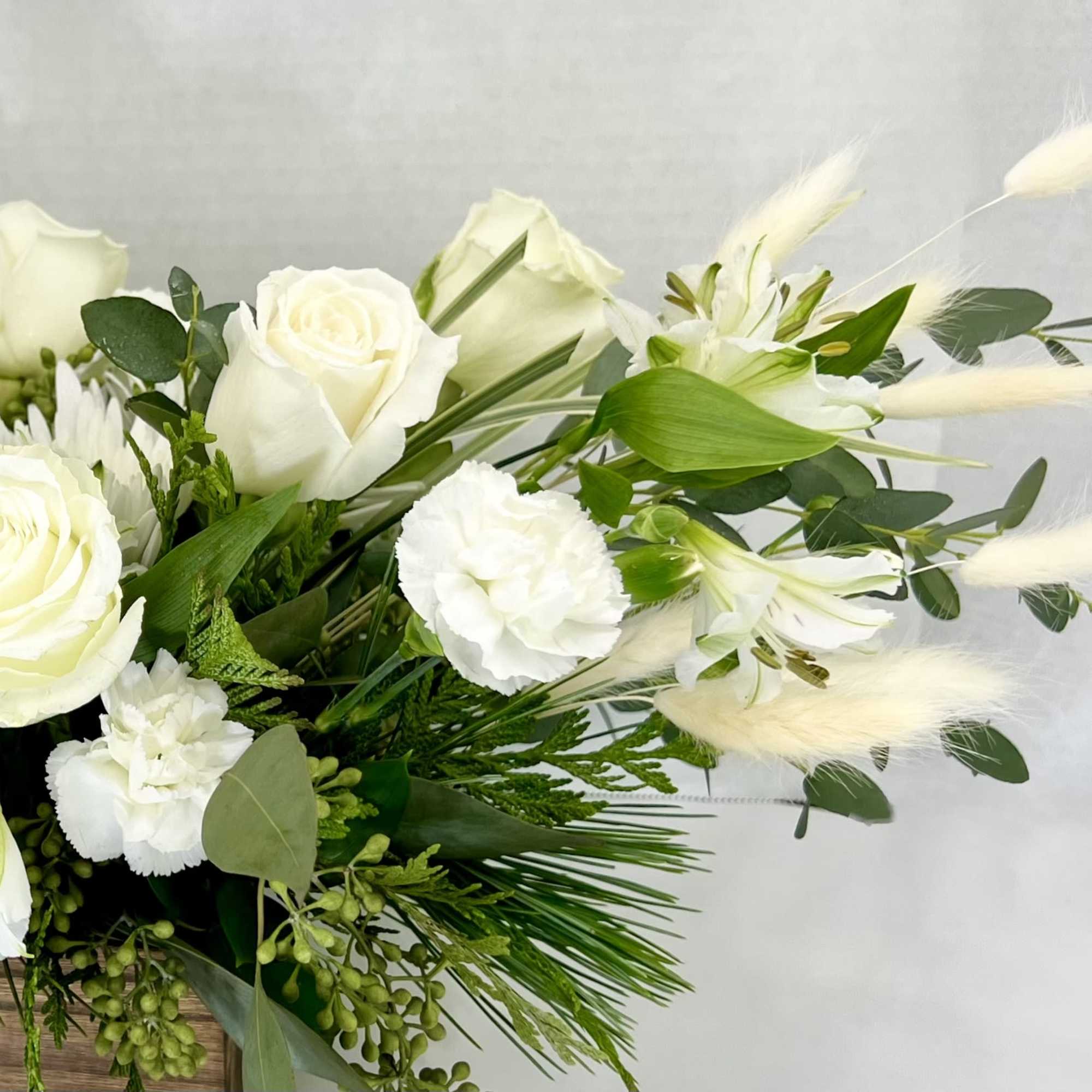 White roses and lilies in a low arrangement with greenery and feathery accents